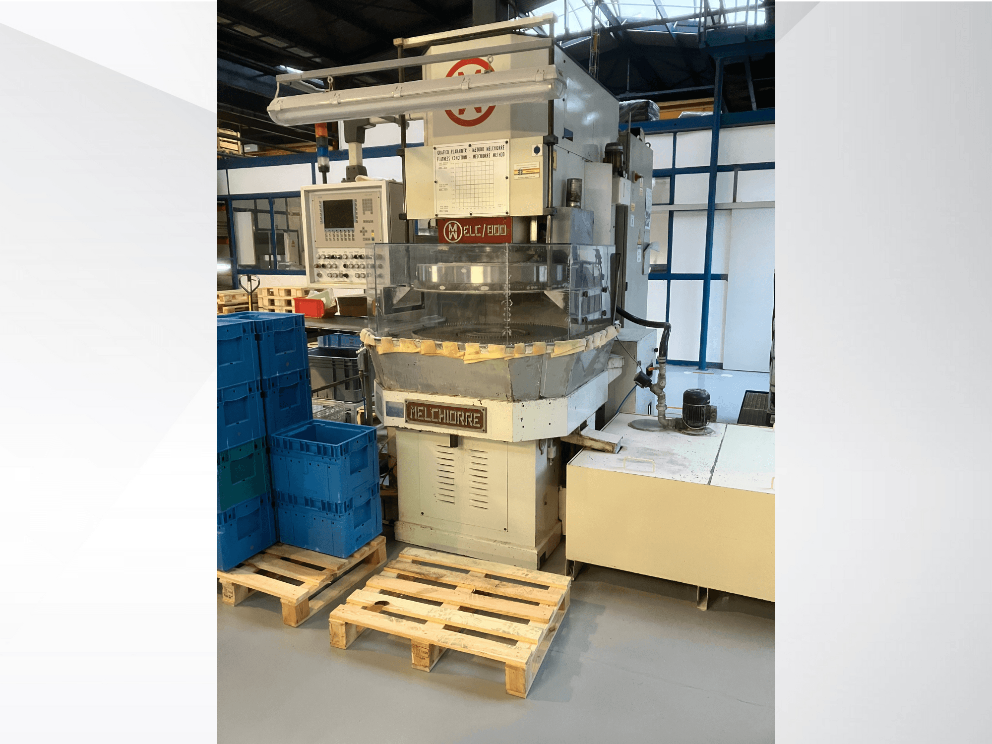 Máquina industrial Melchiorre en vista frontal, con panel de control, tolva transparente y cajas azules sobre palés de madera.