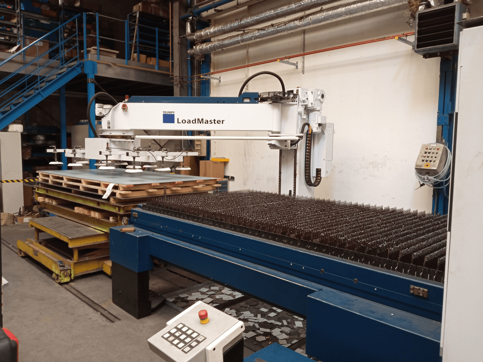 Máquina de corte por láser de CO₂ TRUMPF TruLaser 3030 vista de perfil, con un LoadMaster y palés de materiales.