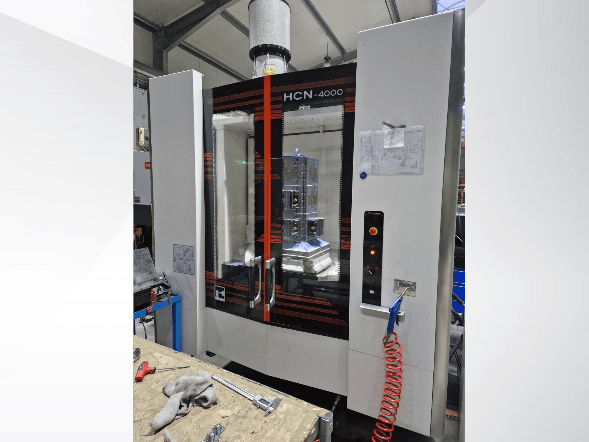 Máquina CNC HCN-4000 en vista frontal, con panel de cristal, panel de control con botones y un plano adjunto.
