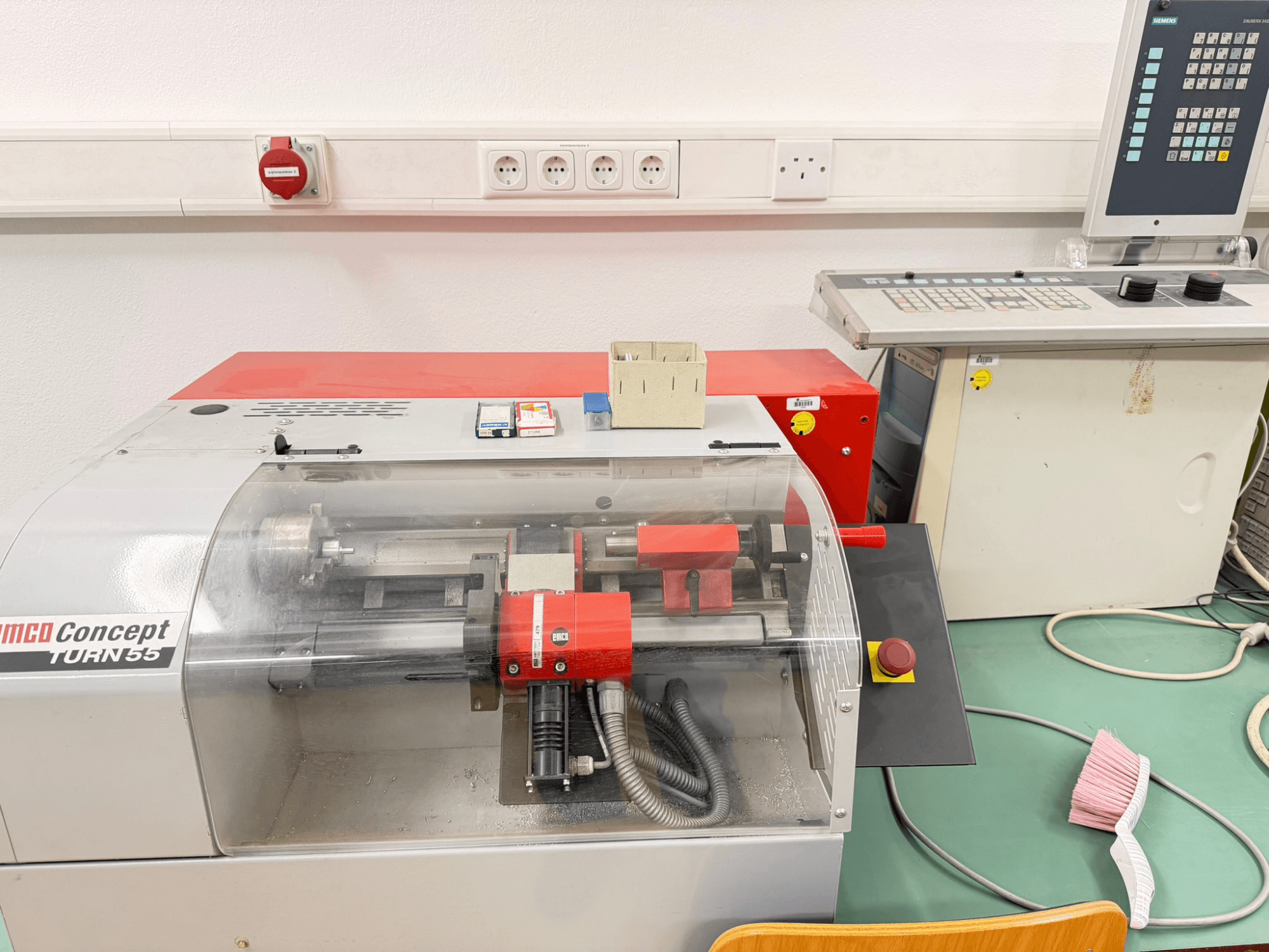 Máquina de torneado horizontal EMCO Concept Turn 55 con exterior rojo y gris, vista frontal que muestra los controles y la zona de trabajo.