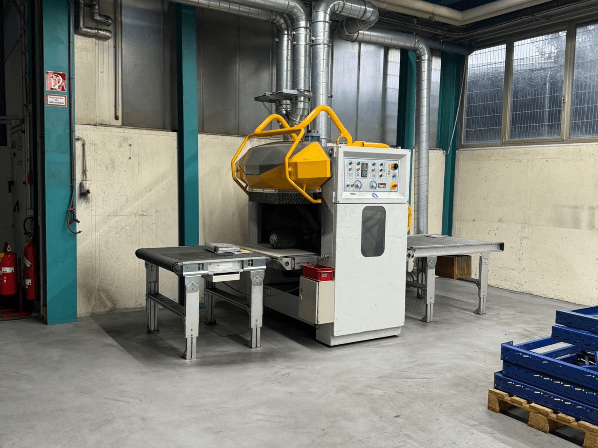 Desbarbadora Fladder AUT-1000 VAC en un entorno de fábrica, con panel de control, protección de seguridad amarilla y mesas de trabajo adyacentes.
