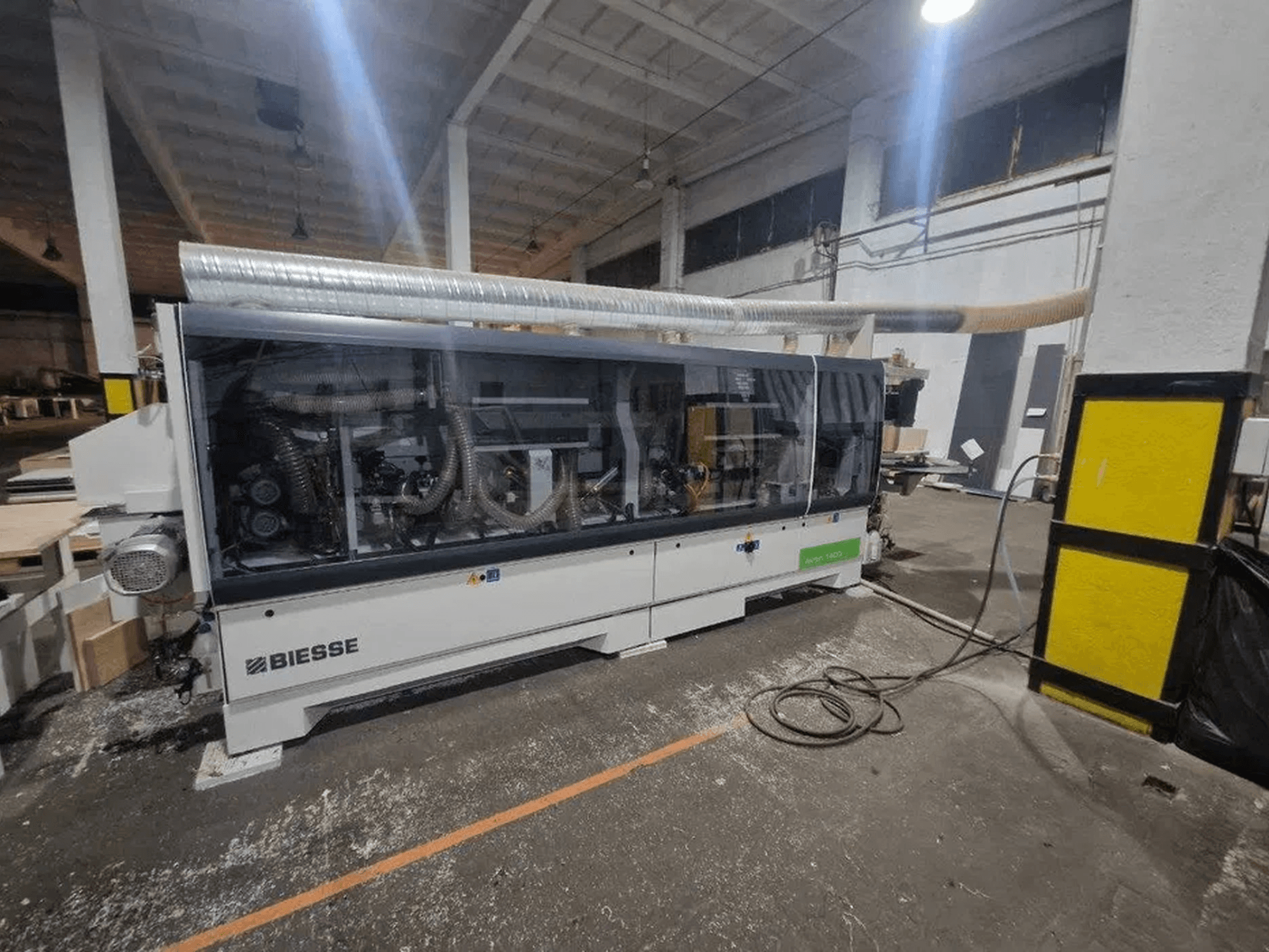 Una encoladora de cantos BIESSE Akron 1440 A en un taller, con una cubierta transparente y los componentes de la máquina a la vista.