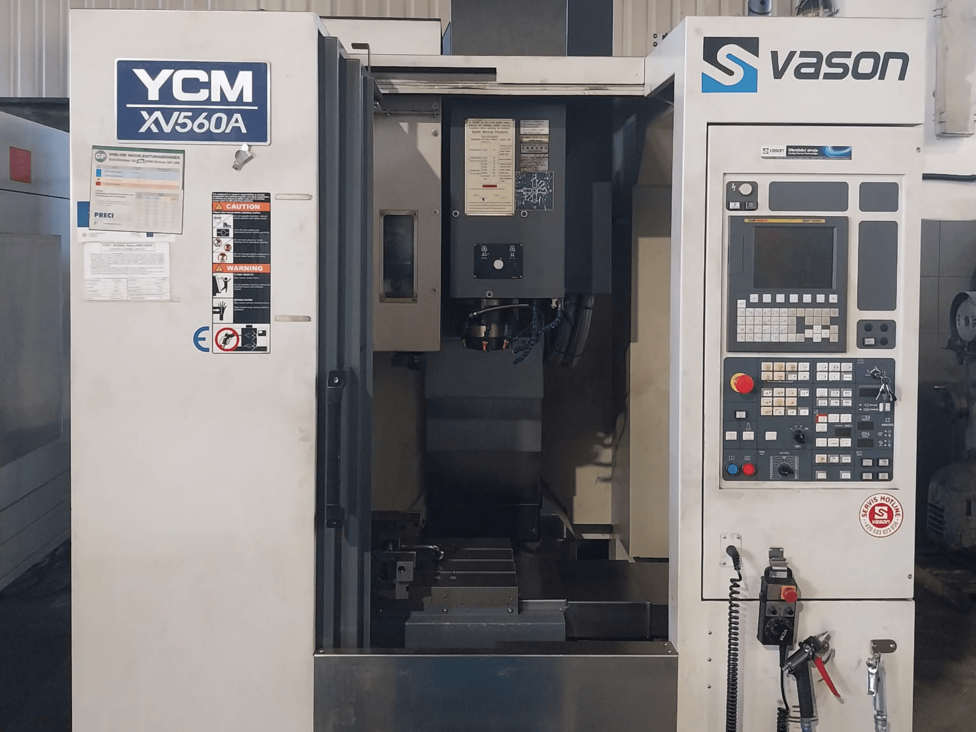 Vista frontal del centro de mecanizado vertical YCM XV 560A, con panel de control y mesa de trabajo con los componentes de mecanizado visibles.