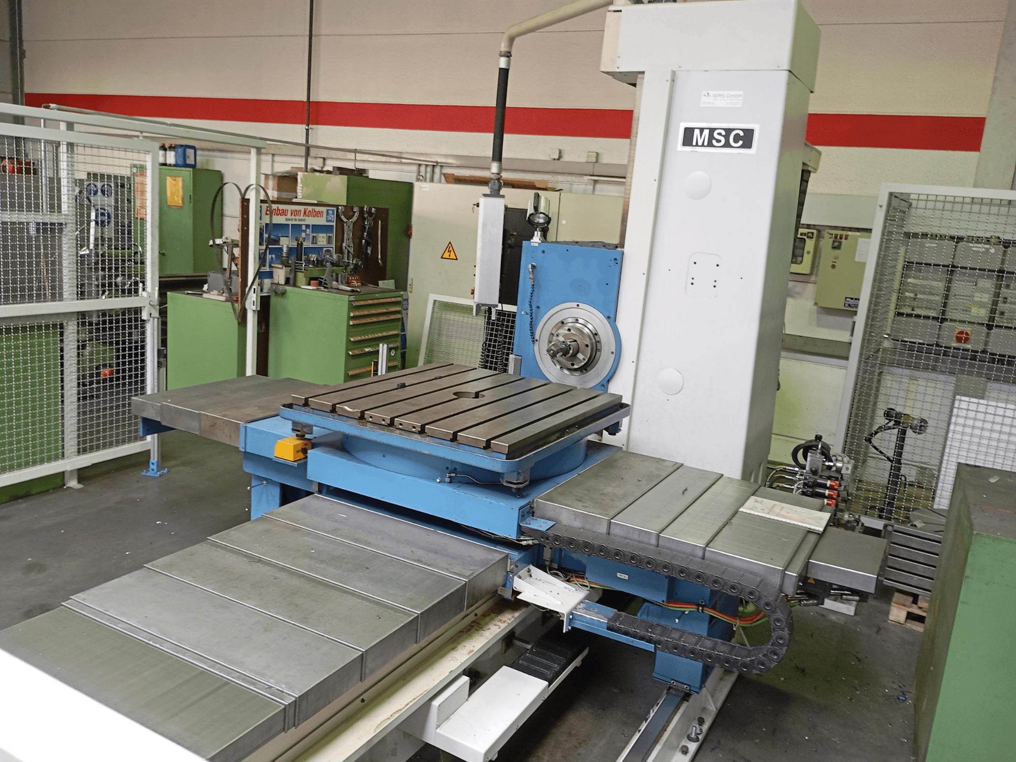 La máquina de mandrinado MSC BFT 90/5 TNC 320, vista lateral, cuenta con una mesa de trabajo metálica y un portaherramientas en un entorno de taller.