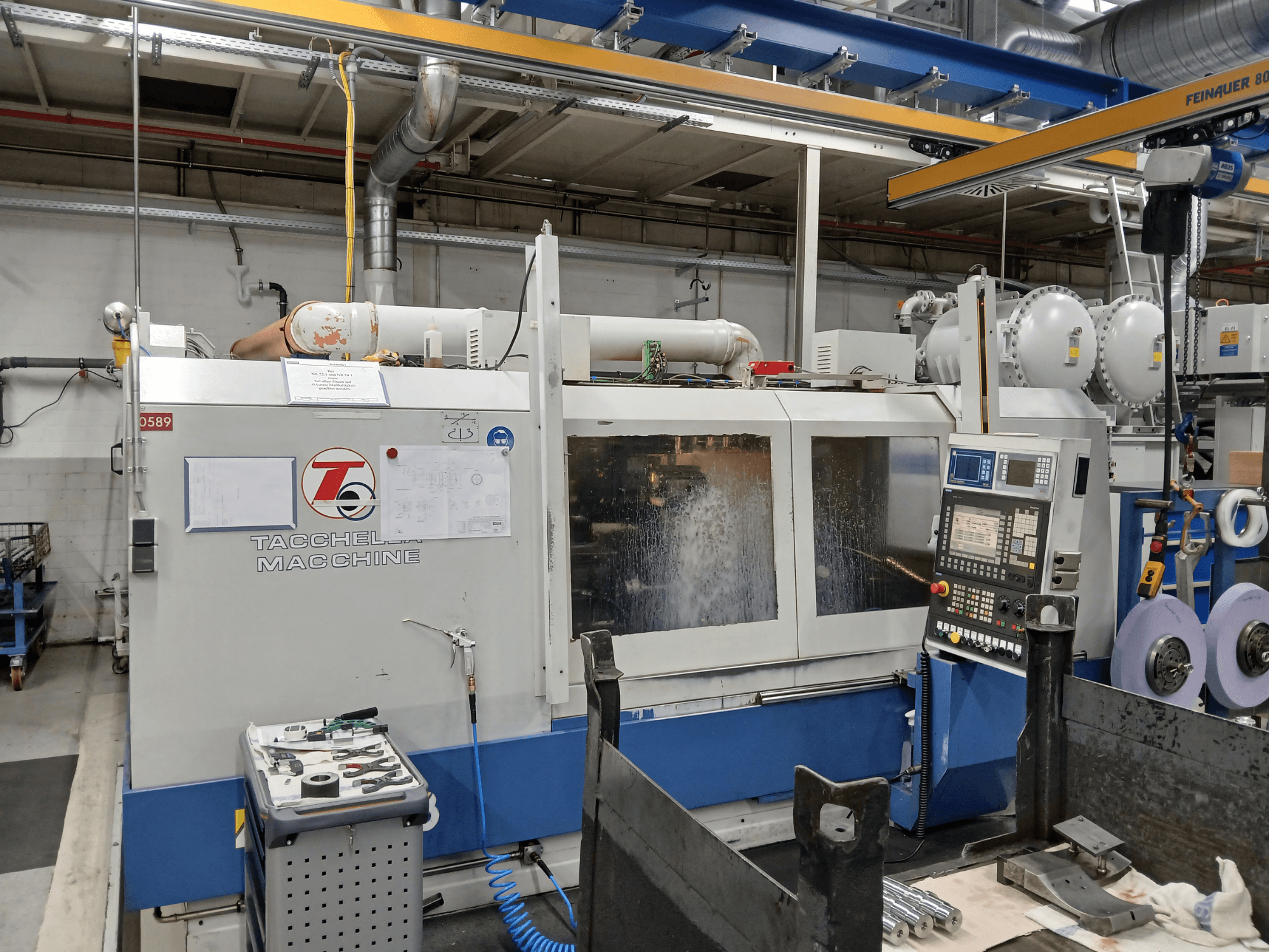 Centro de mecanizado Tacchella desde una vista frontal, con el panel de control y las herramientas visibles. Salpicaduras de refrigerante de agua durante el funcionamiento.