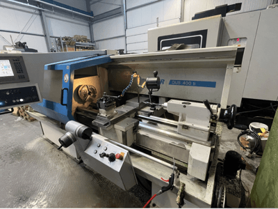 Máquina de torno CNC DUS 400 ti desde la vista frontal, con panel de control, portaherramientas y espacio de trabajo iluminado.