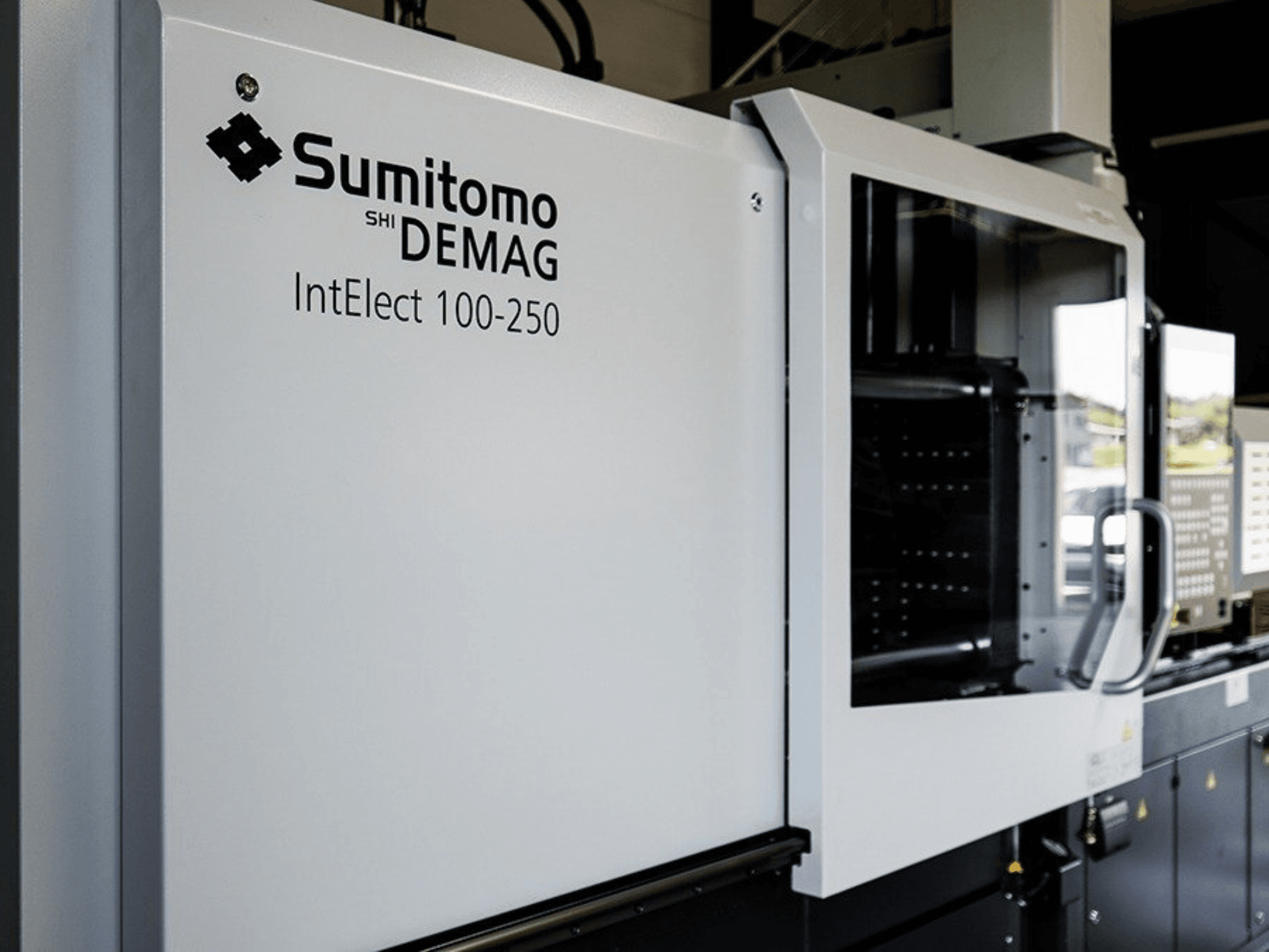 Vista frontal de la máquina de moldeo por inyección eléctrica SUMITOMO SHI DEMAG IntElect 100/250, con panel de control y dispositivos de seguridad.