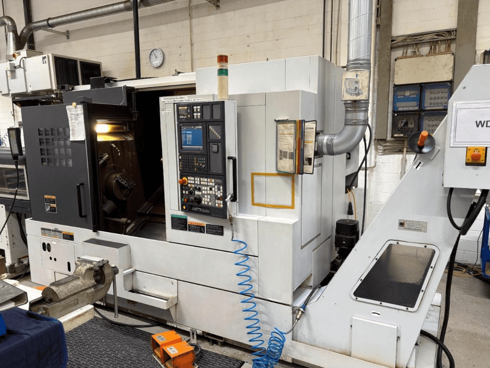Centro de torneado y fresado MORI SEIKI NL 2500 SY, vista frontal, mostrando el panel de control y la zona de mecanizado. Sistema de refrigeración y accesorios visibles.