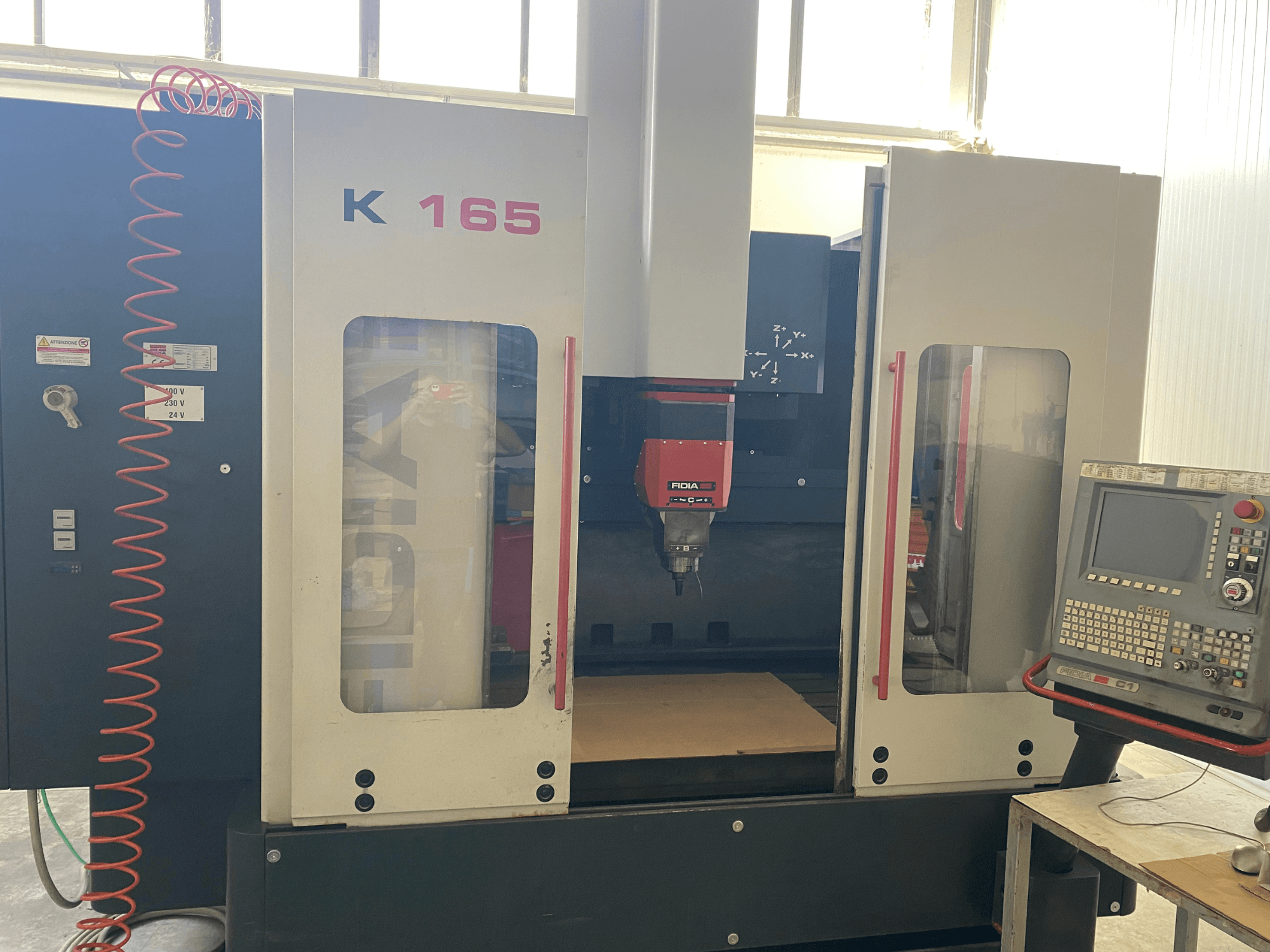 Máquina CNC Fidia K 165 con husillo rojo y panel de control, vista de frente, en un taller bien iluminado.