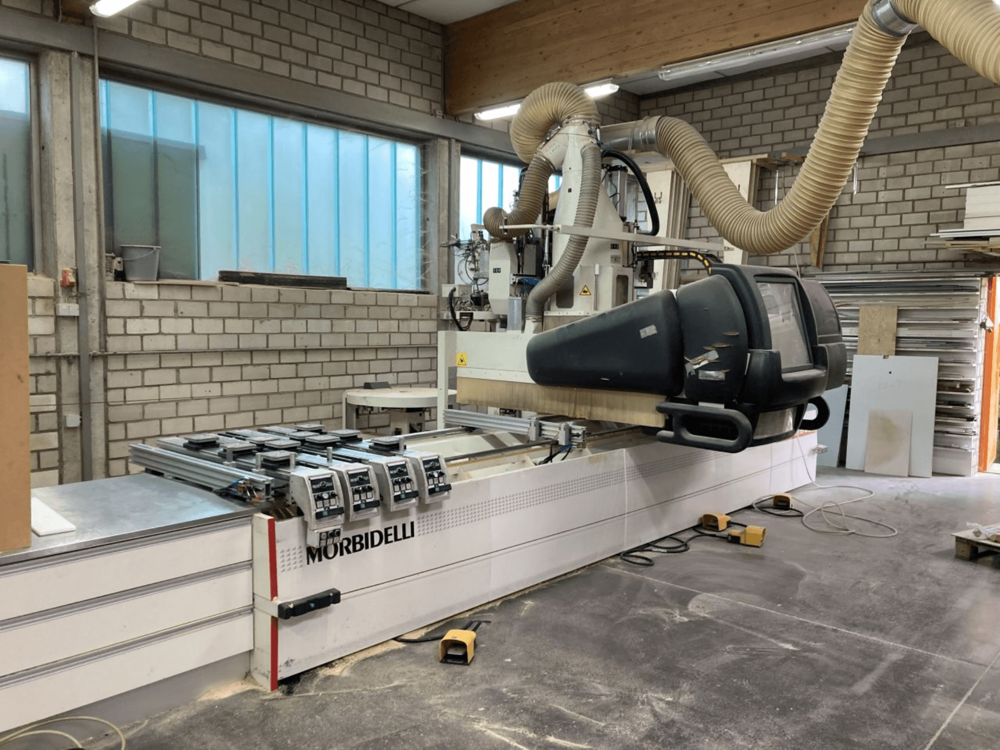 Máquina CNC MORBIDELLI en un taller, vista frontal con panel de control, sistema de extracción de polvo y pieza de madera posicionada.