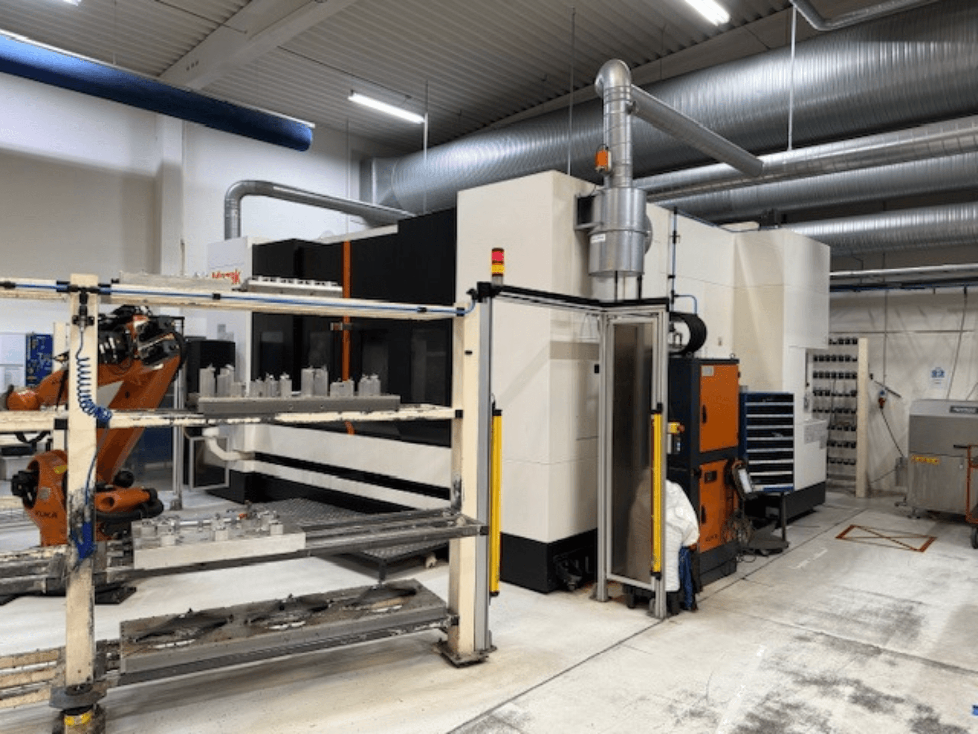 Máquina CNC industrial con brazo robotizado y barreras de seguridad, con una vista frontal de la configuración en un espacio de trabajo aireado.