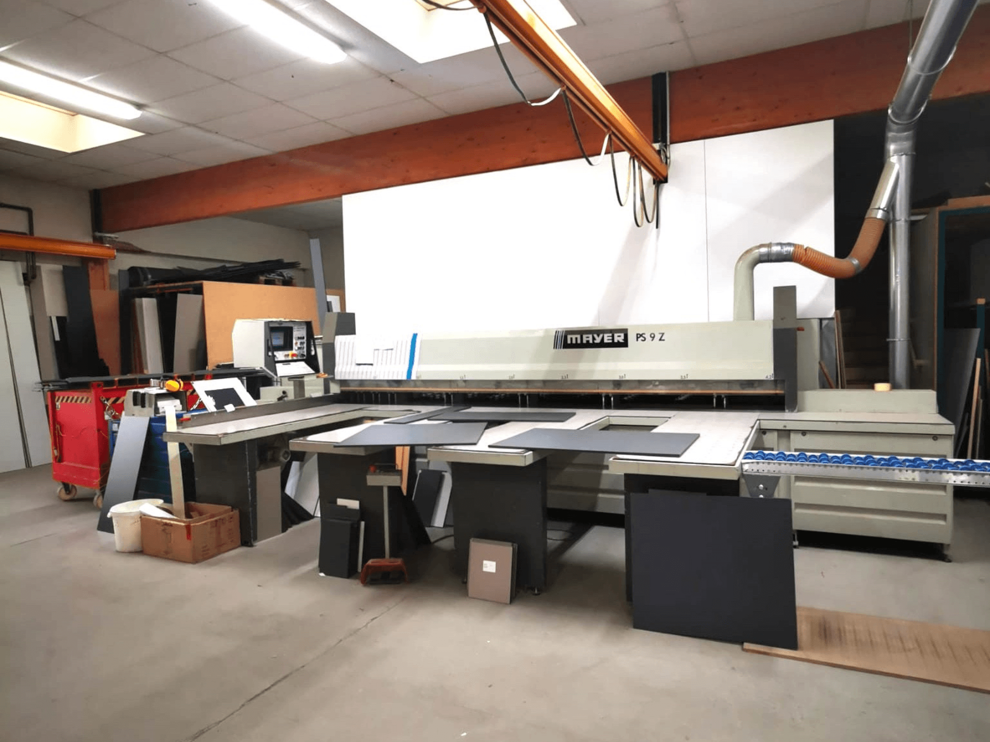Máquina de corte MAYER PS9 Z en un taller, vista frontal, con varios materiales y un sistema de transporte visibles.
