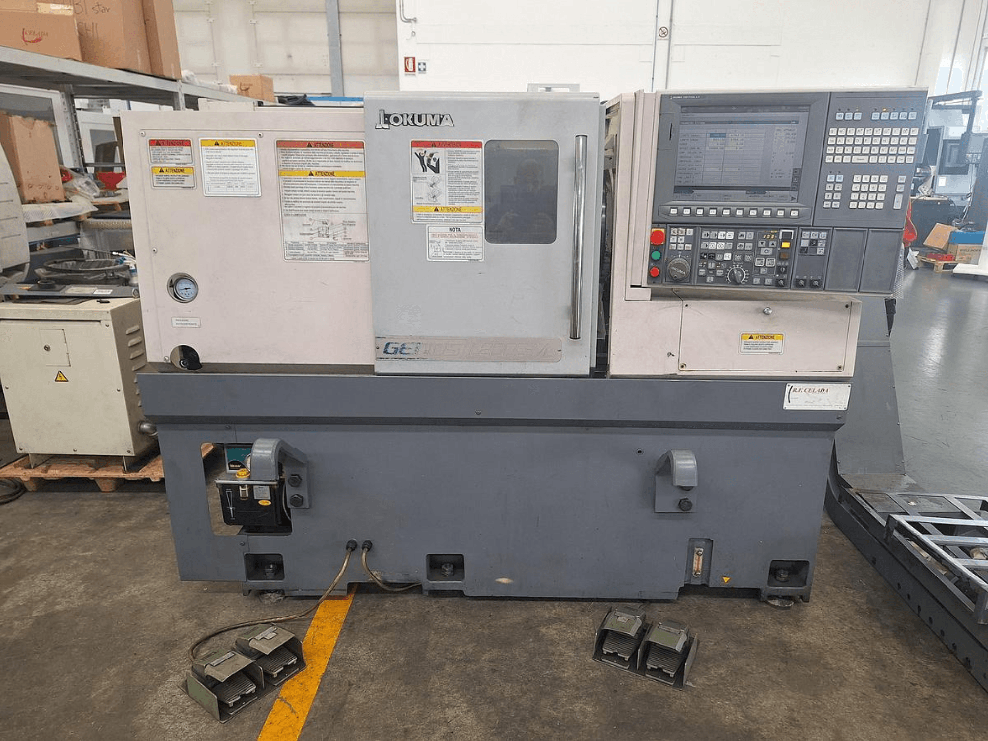 Tornos horizontales Okuma GENOS L200E-M en vista lateral; incluye panel de control, advertencias de seguridad y pedales.