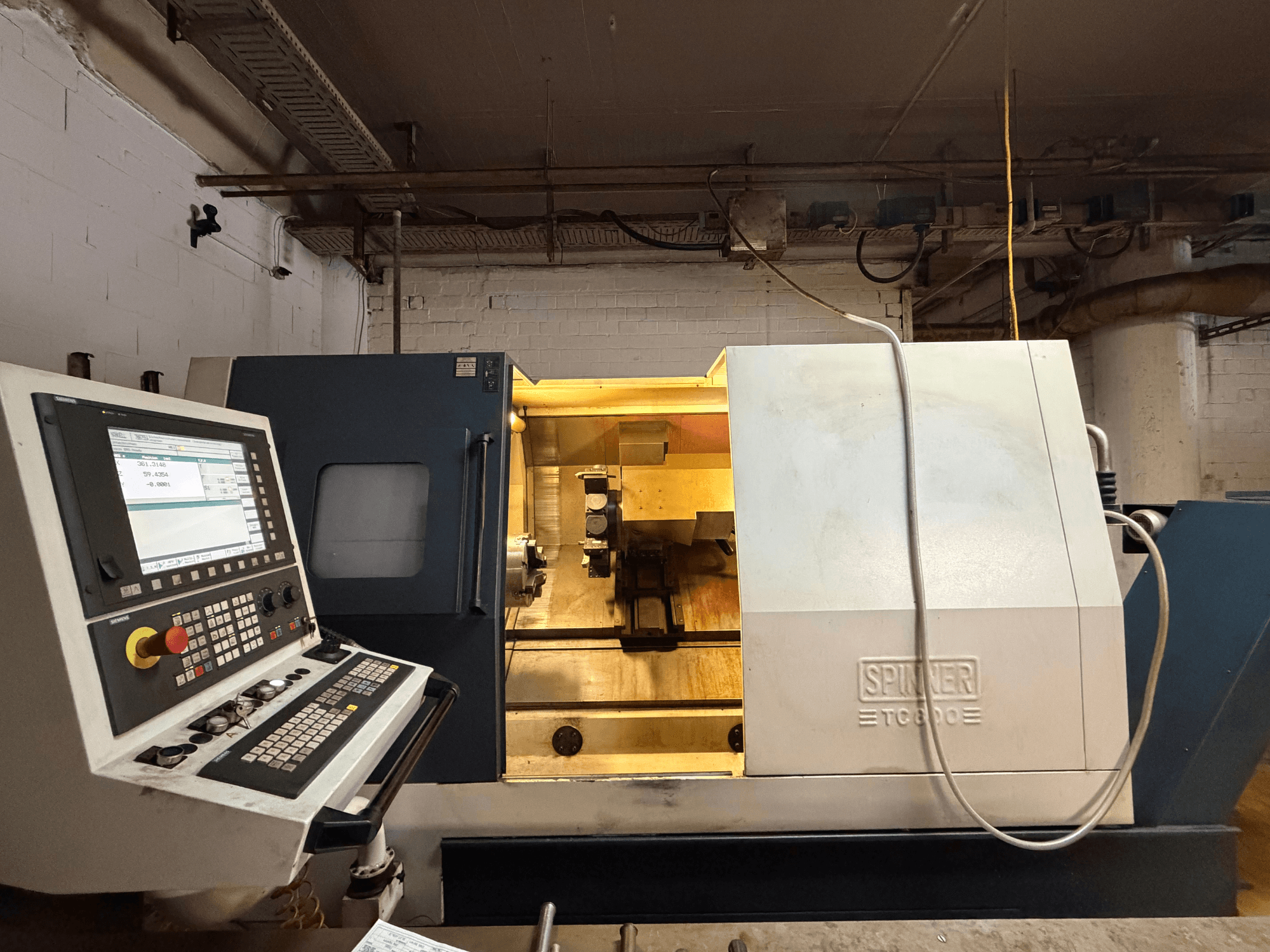 Máquina de torneado horizontal SPINNER TC800 en un taller, con panel de control y componentes internos visibles.