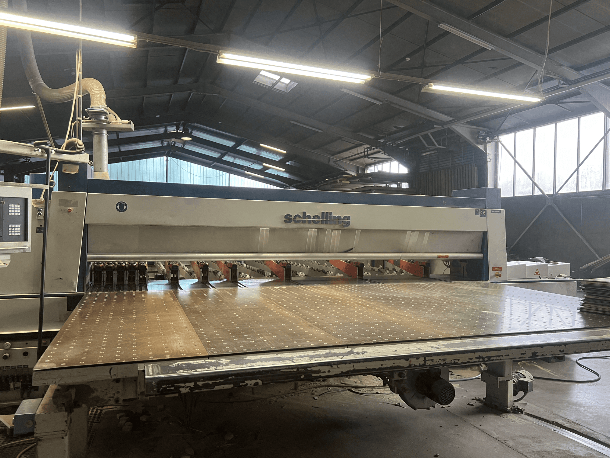 Vista frontal de la seccionadora Schelling, con una gran mesa de corte perforada y múltiples cuchillas para un corte preciso de la madera.