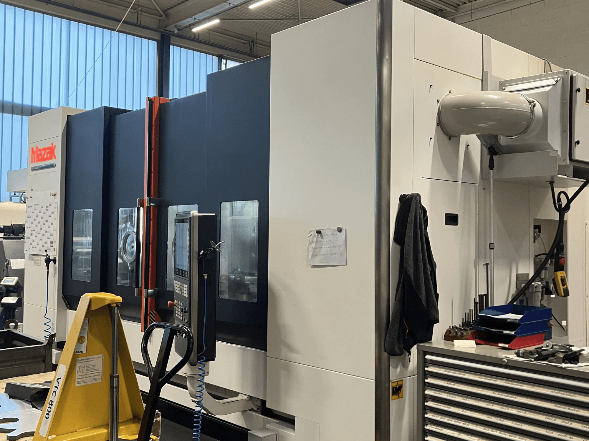 Máquina CNC Mazak vista desde un lateral, mostrando el panel de control y las características de seguridad en un entorno de taller.