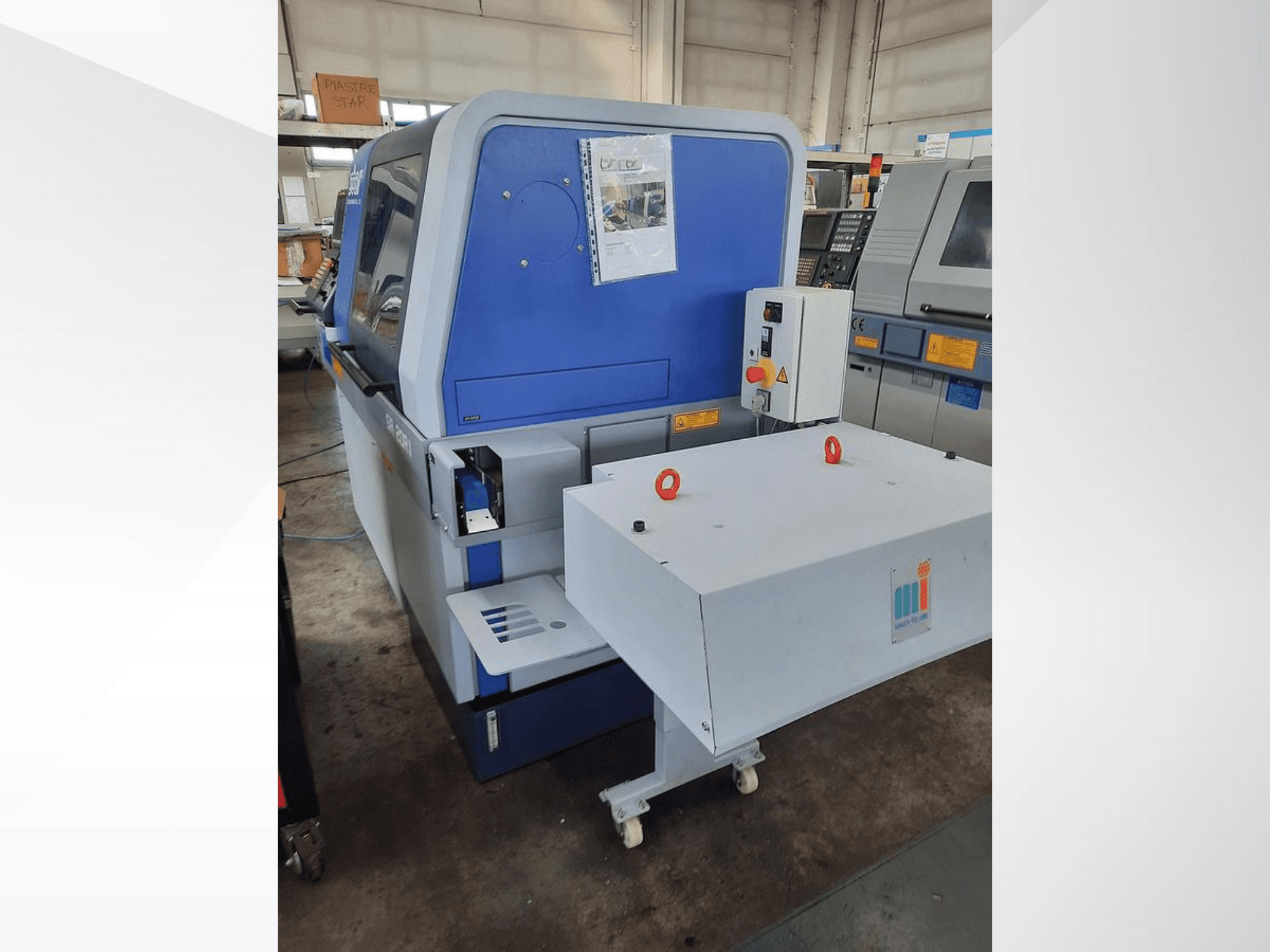 Máquina industrial azul con un transportador blanco, mostrando el panel de control y los dispositivos de seguridad adjuntos, vista lateral.