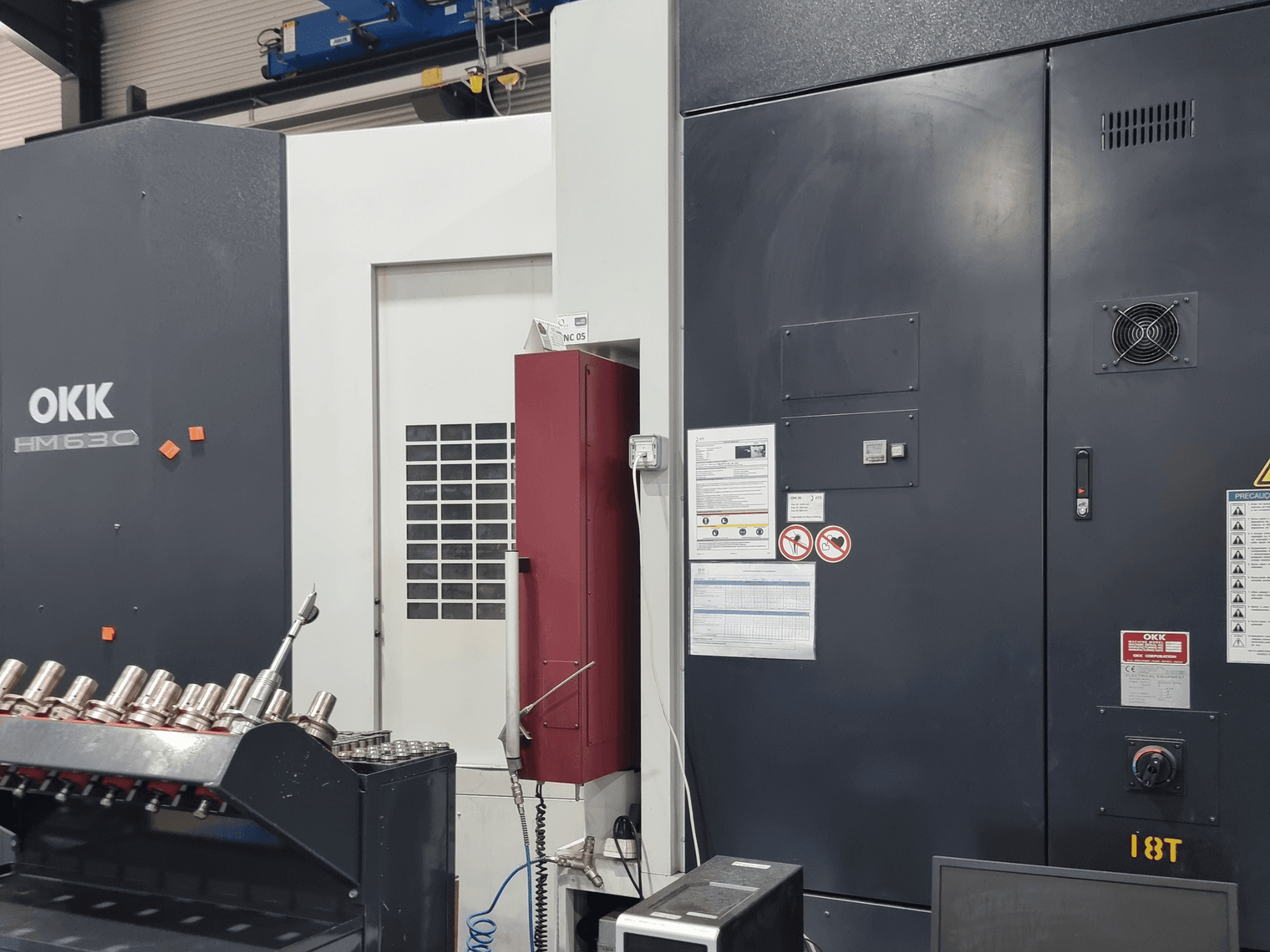 Centro de mecanizado horizontal OKK HM630, vista frontal en la que se aprecian el panel de control, las indicaciones de seguridad y el compartimento para herramientas situado en el lateral.