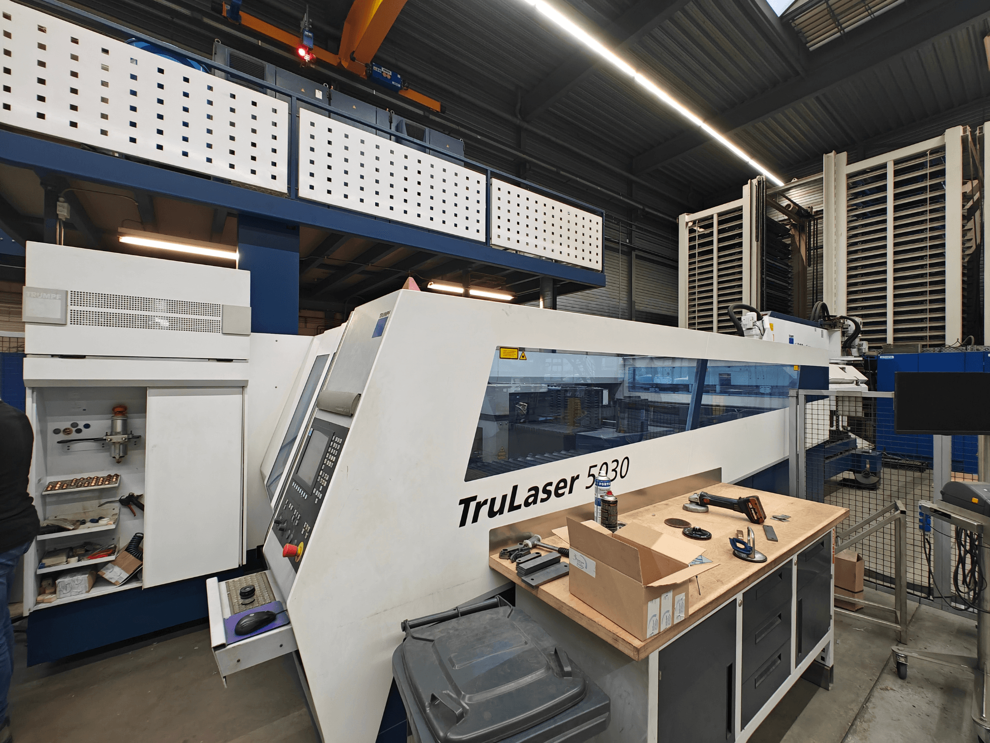 Máquina TruLaser 5030 en un taller, vista frontal con panel de control visible, rodeada de herramientas y equipos.