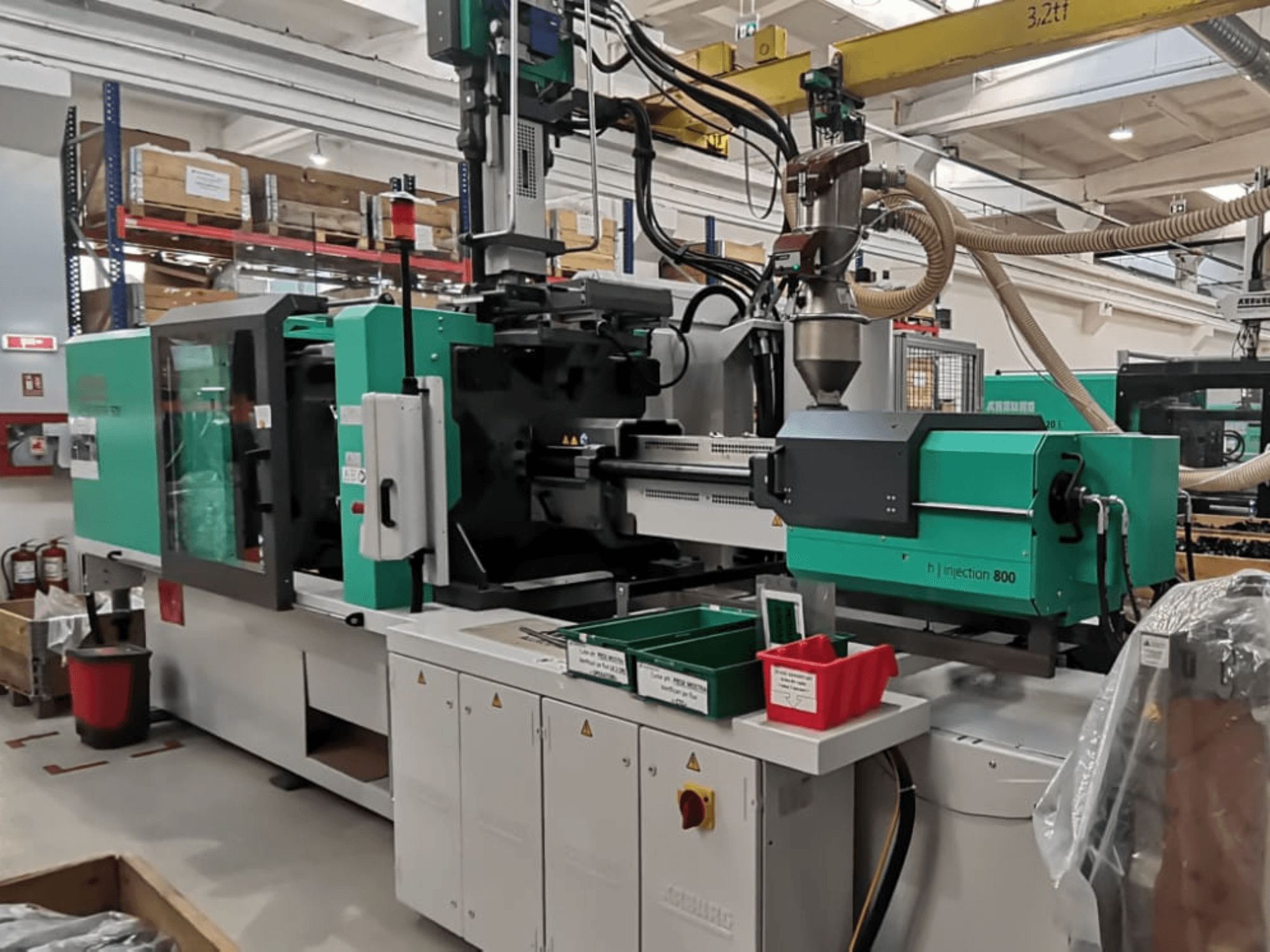 Máquina de inyección H 800 en una fábrica, vista frontal, de diseño verde y negro, con paneles de control y contenedores para piezas.