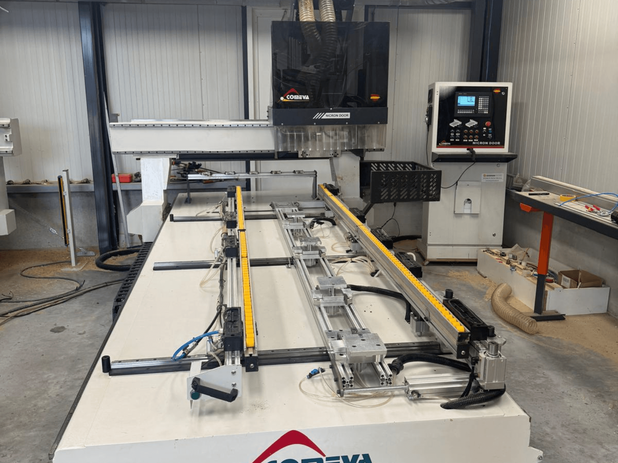 Vista frontal del centro de mecanizado de madera CNC COMEVA MEX V 2100x3260, que cuenta con una estación de trabajo, un panel de control y unos carriles guía.