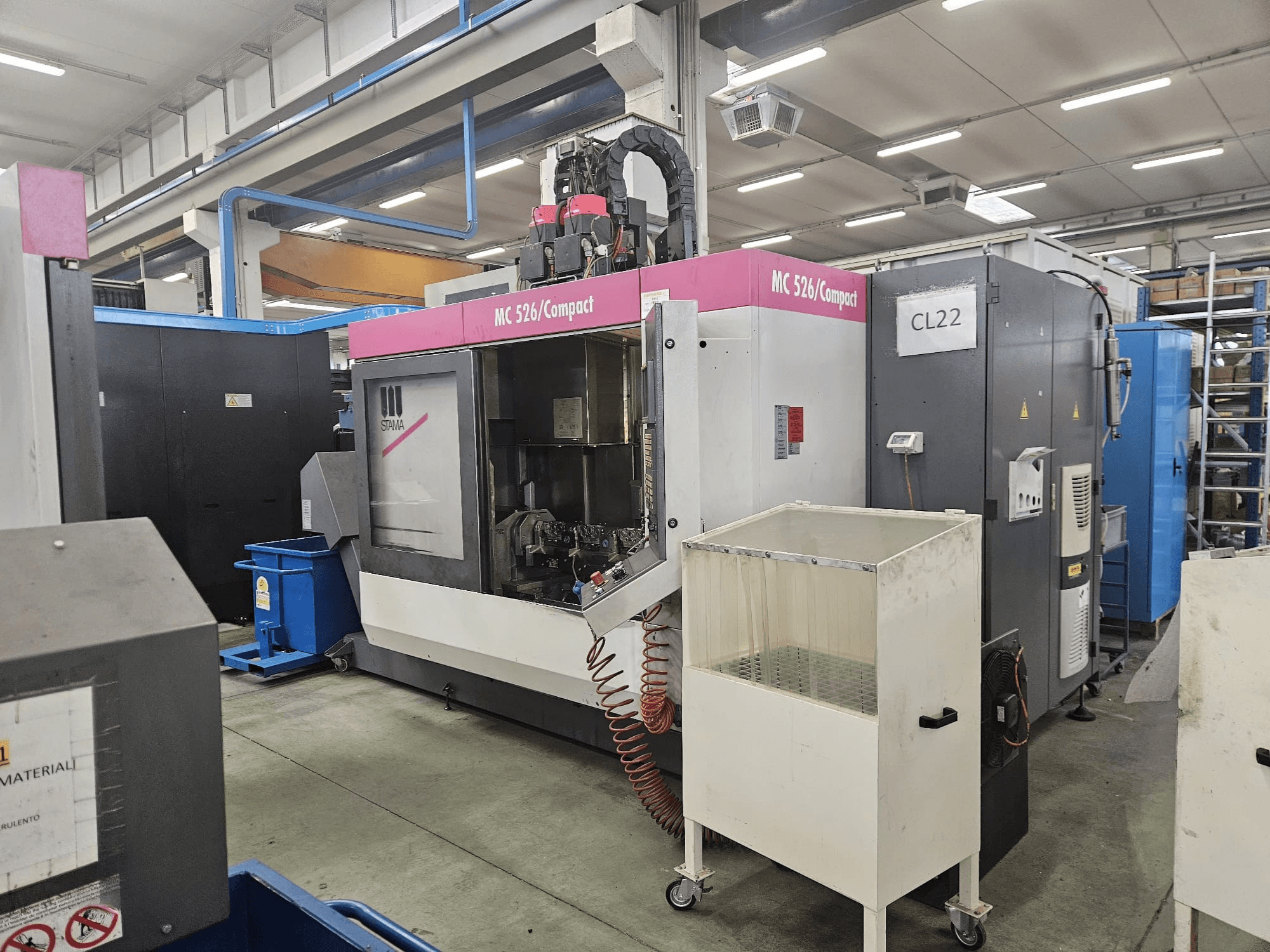 Máquina CNC compacta MC 526 de Stama, vista lateral, mostrando el panel de control, el depósito de refrigerante y la maquinaria adyacente.