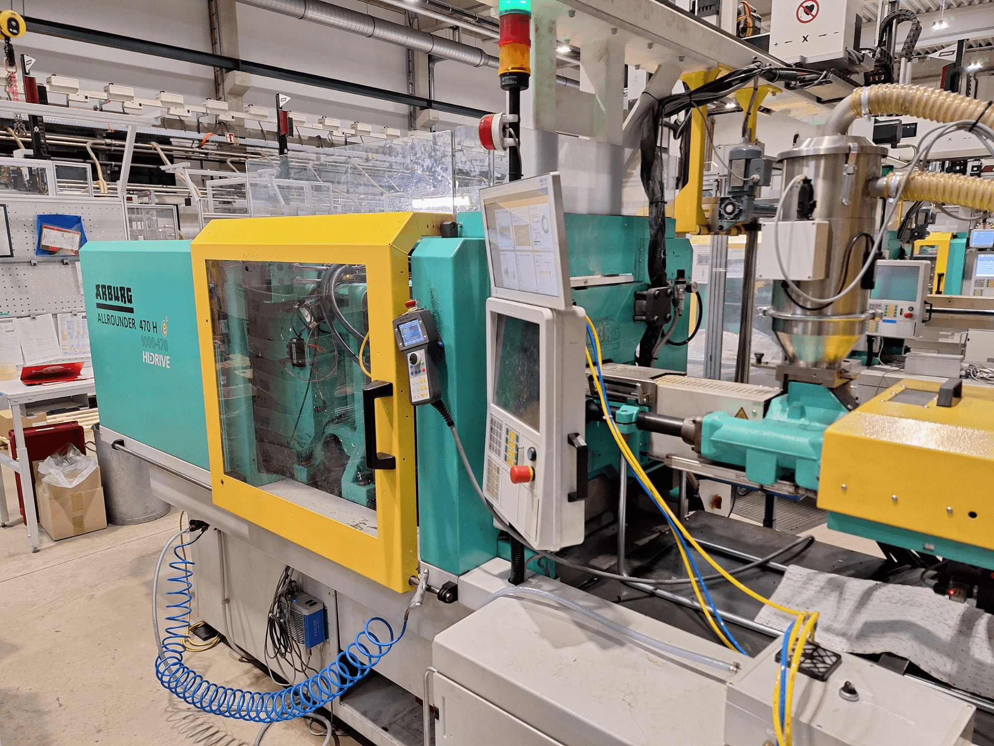 Máquina de moldeo por inyección hidráulica Arburg 470 H 1000-170, vista lateral que muestra el panel de control y el sistema de alimentación.