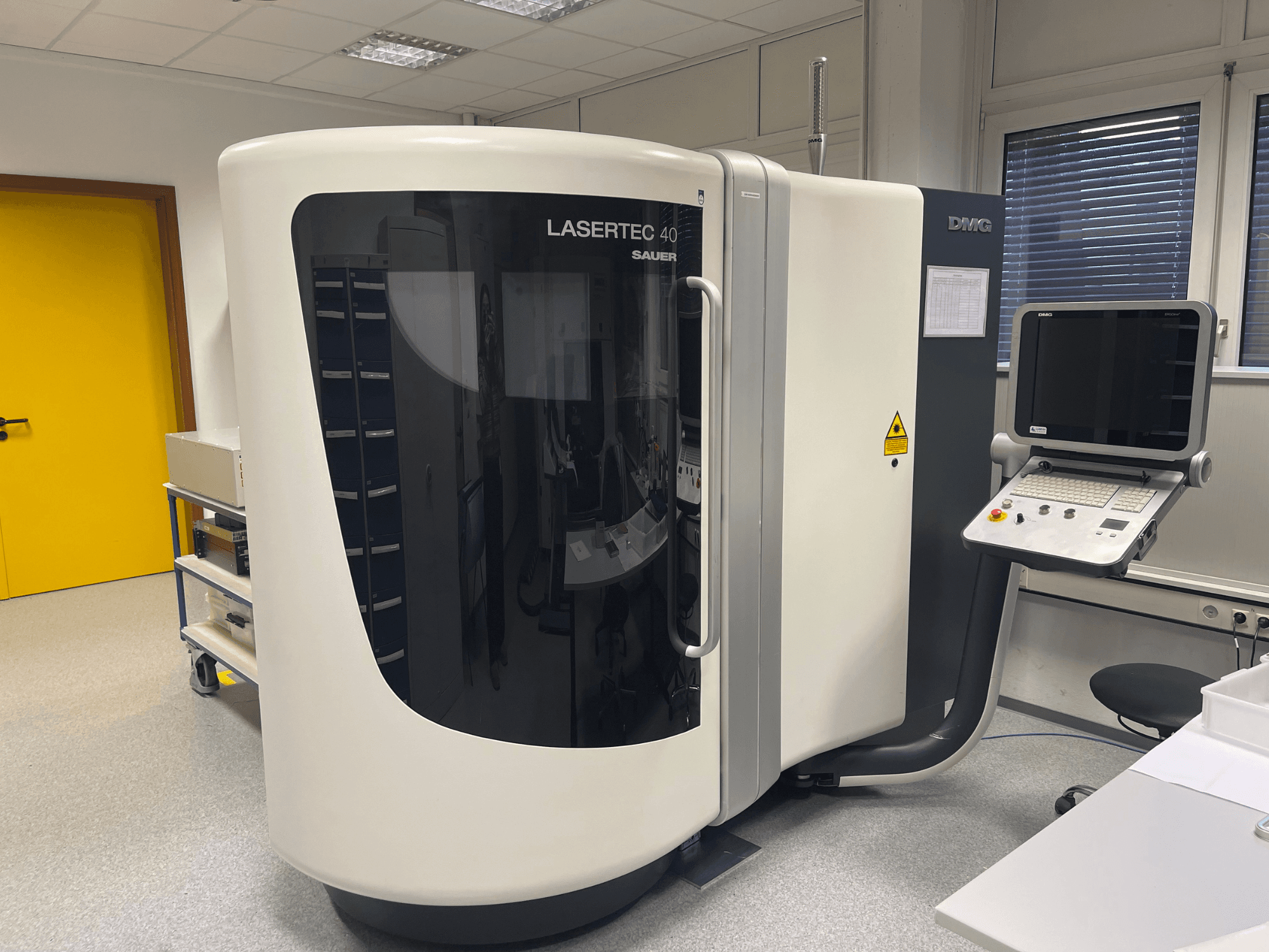 Fresadora LASERTEC 40 blanca de DMG MORI, vista frontal, con panel de control y diseño ergonómico en una sala bien iluminada.