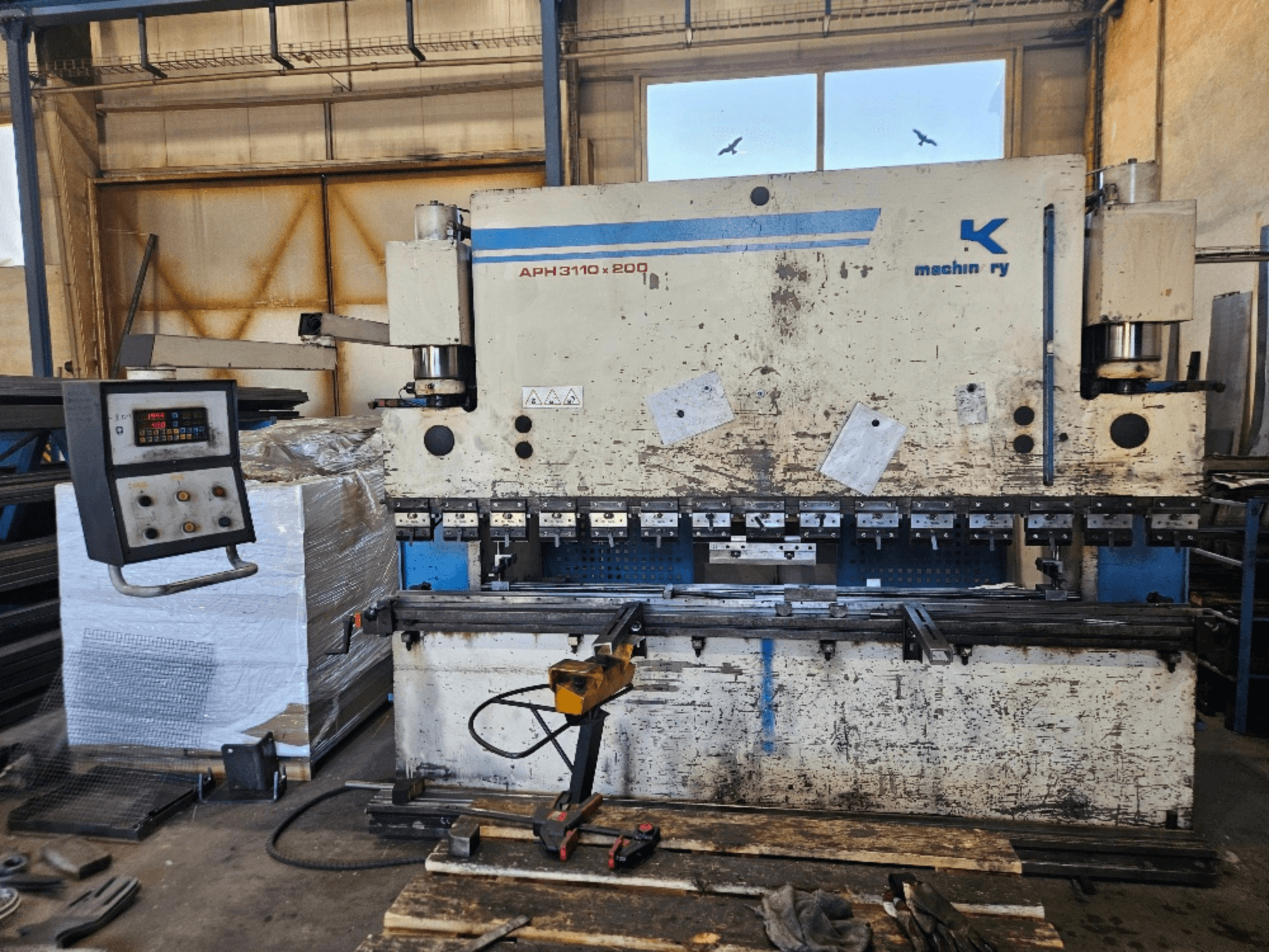 Plegadora Baykal APH 3110x200 en un taller, vista frontal, con panel de control, chapas y herramientas visibles.