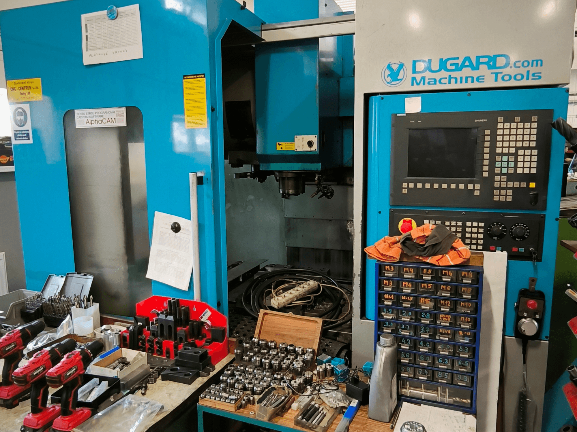 Vista frontal del centro de mecanizado vertical Dugard 850VMC, que muestra el panel de control, las herramientas y los accesorios en un banco de trabajo.