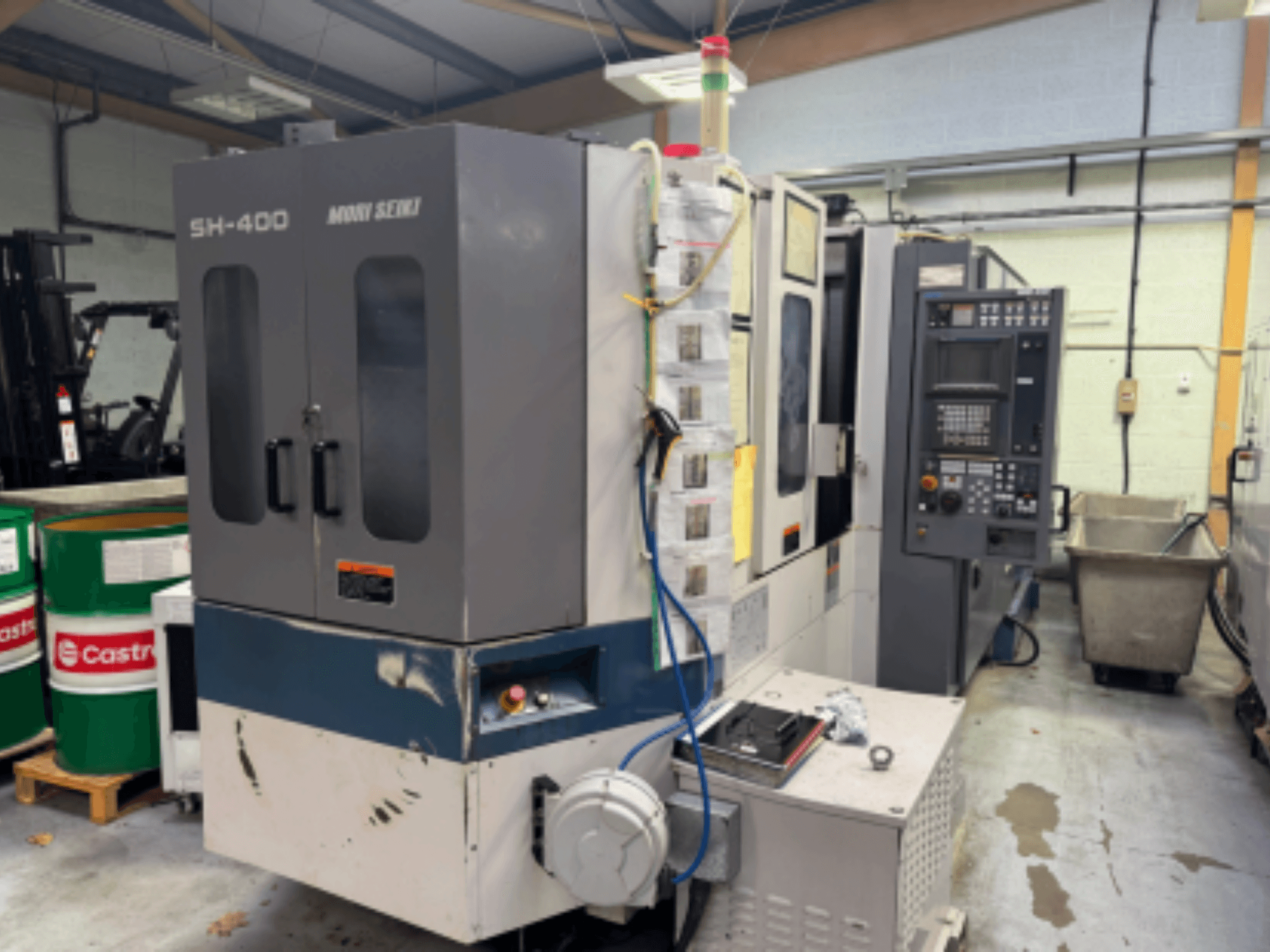 Máquina CNC SH-400 de Moni Seiki, vista lateral que muestra el panel de control, las puertas y el entorno industrial circundante.