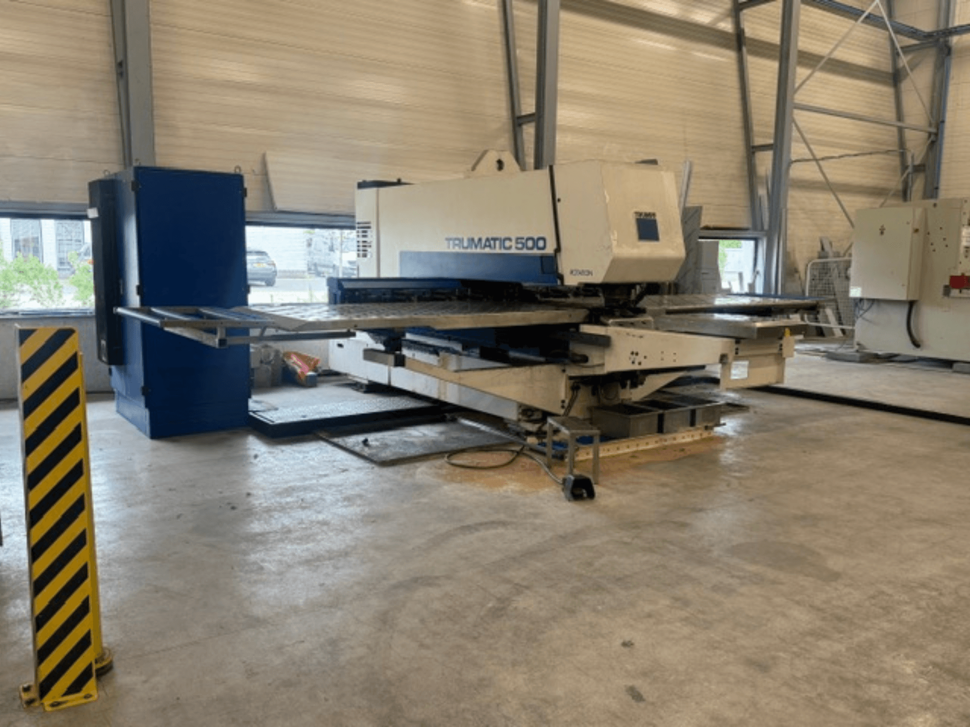 Punzonadora CNC TRUMPF Trumatic 500 en un taller; vista lateral en la que se aprecian la máquina y el poste de seguridad con rayas amarillas.