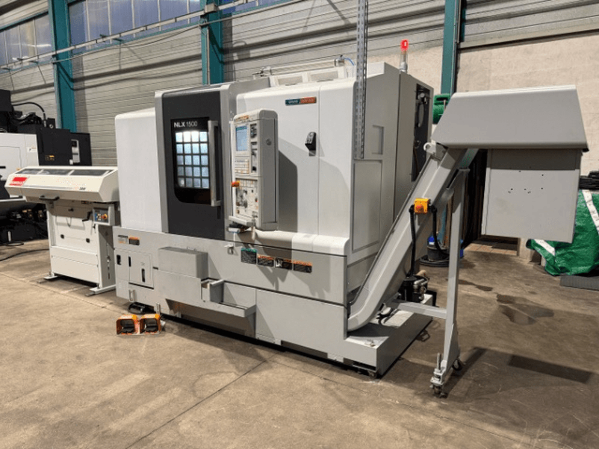 Máquina CNC NLK 1500, vista frontal, con panel de control y tolva de accesorios en el lateral, apoyada sobre suelo de hormigón.