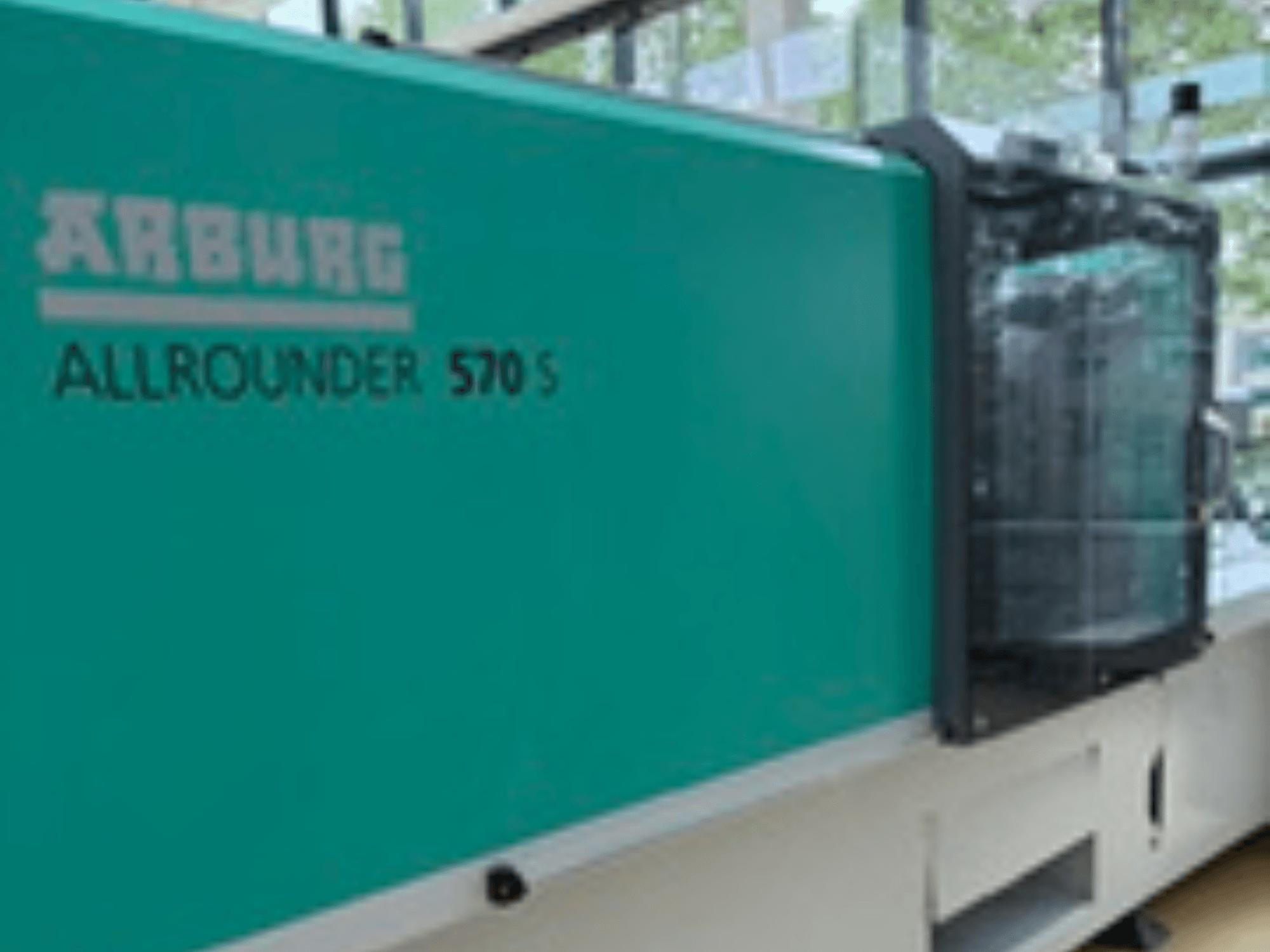Vista frontal de la ALLROUNDER 570 S 1600-290 de Arburg, con exterior y unidad de inyección de color verde azulado, que muestra parte del diseño de la máquina.