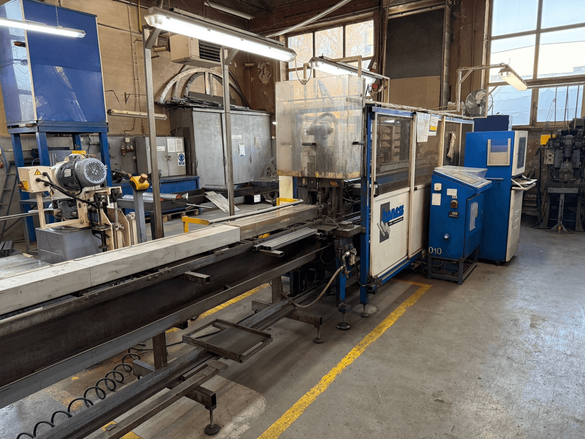 Taller industrial con una máquina Haweas azul, vista lateral que muestra el transportador y el equipo en un espacio amplio y bien iluminado.