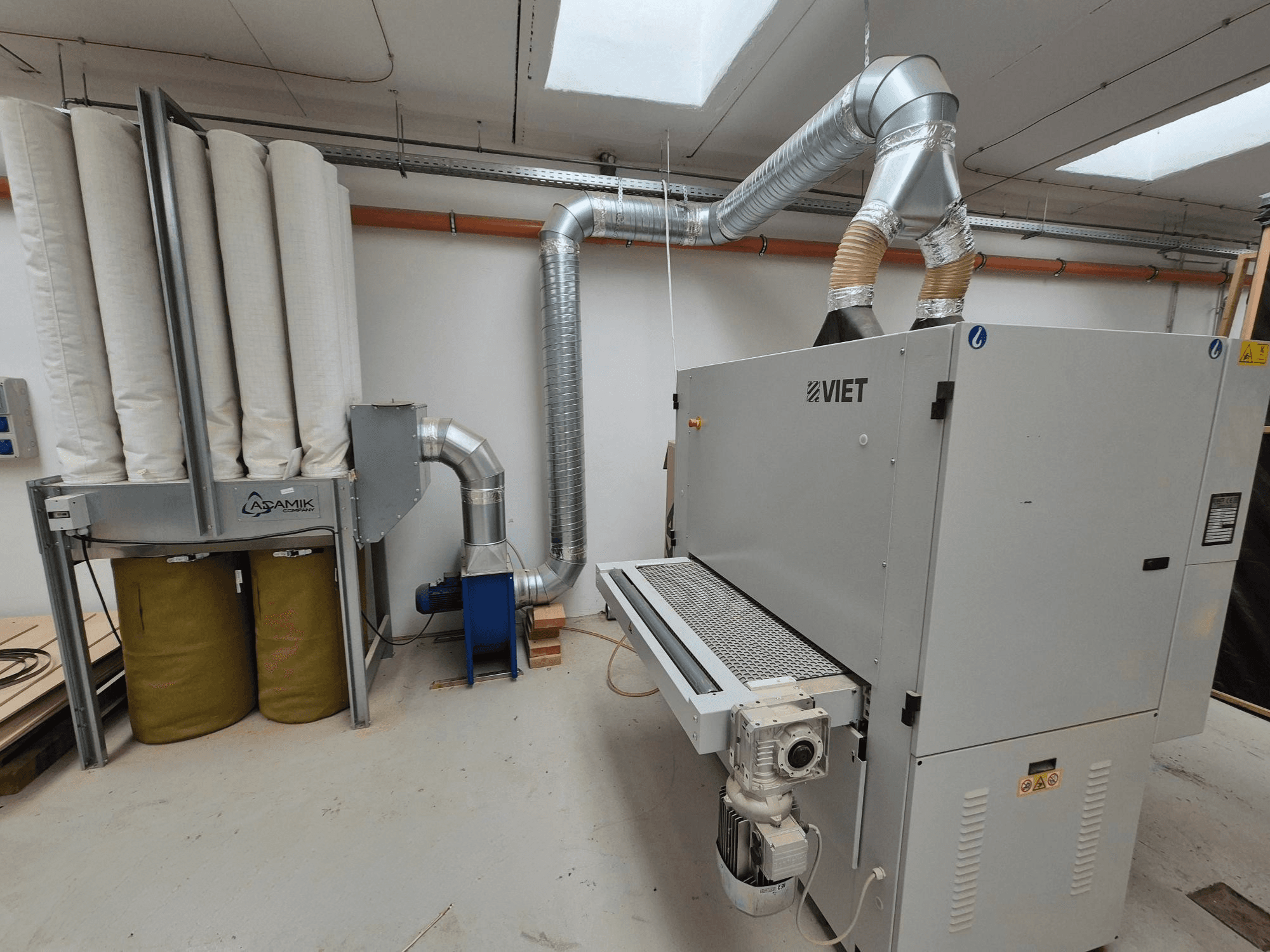 Sistema de aspiración de polvo Viet con filtros cilíndricos y un tubo de escape plateado, visto de frente en un taller.