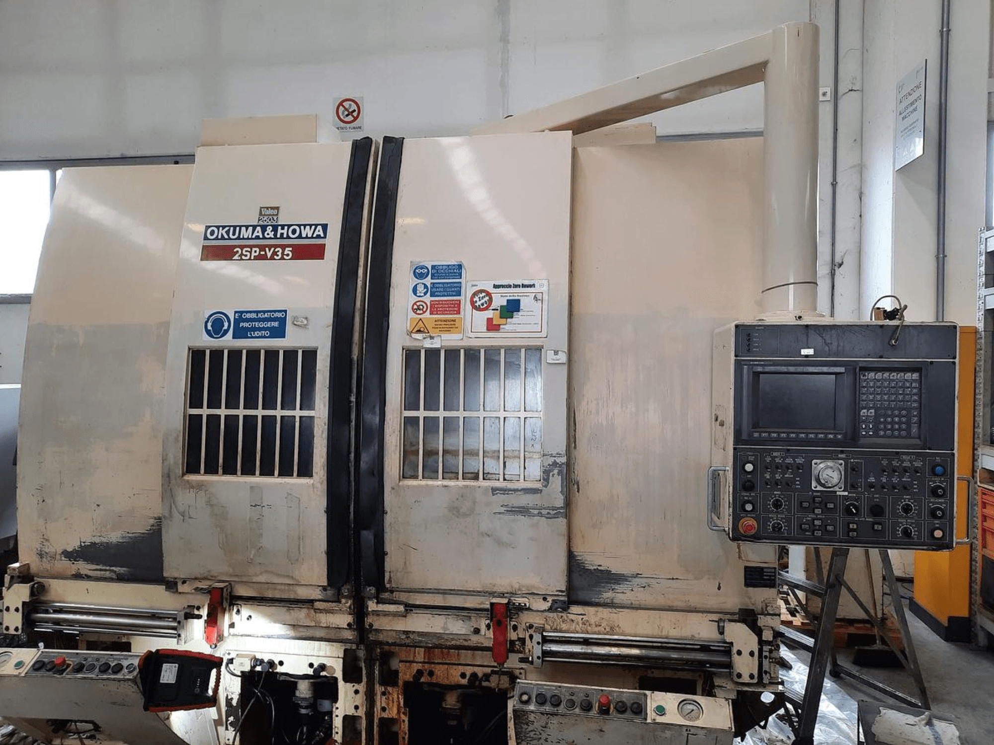 Máquina CNC OKUMA & HOWA 2SP-V35 vista de frente, con panel de control con varios botones y etiquetas de seguridad.