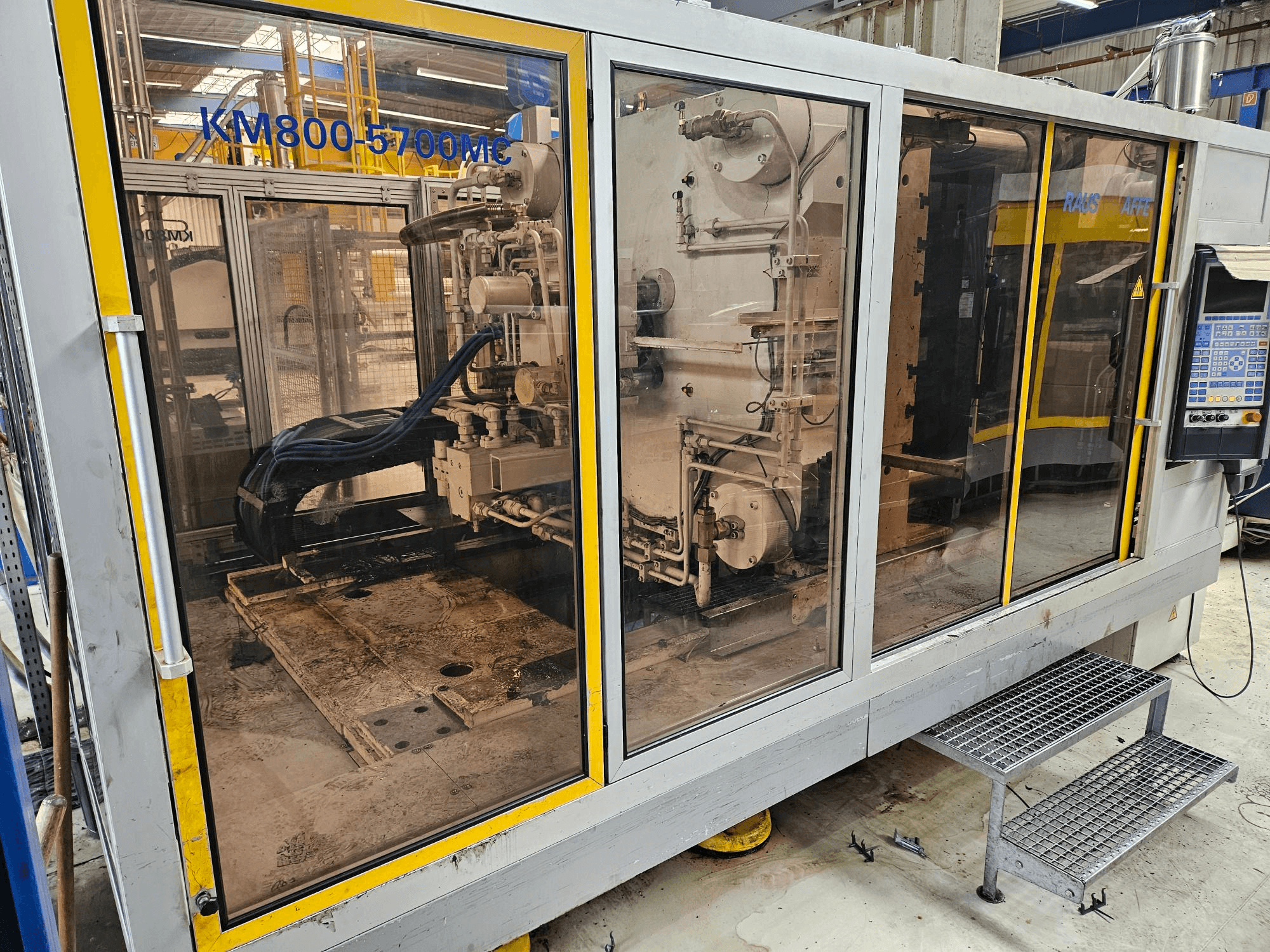 Máquina de moldeo por inyección hidráulica Krauss Maffei KM800-5700 MC, vista frontal en la que se aprecian los componentes a través de los paneles de cristal.