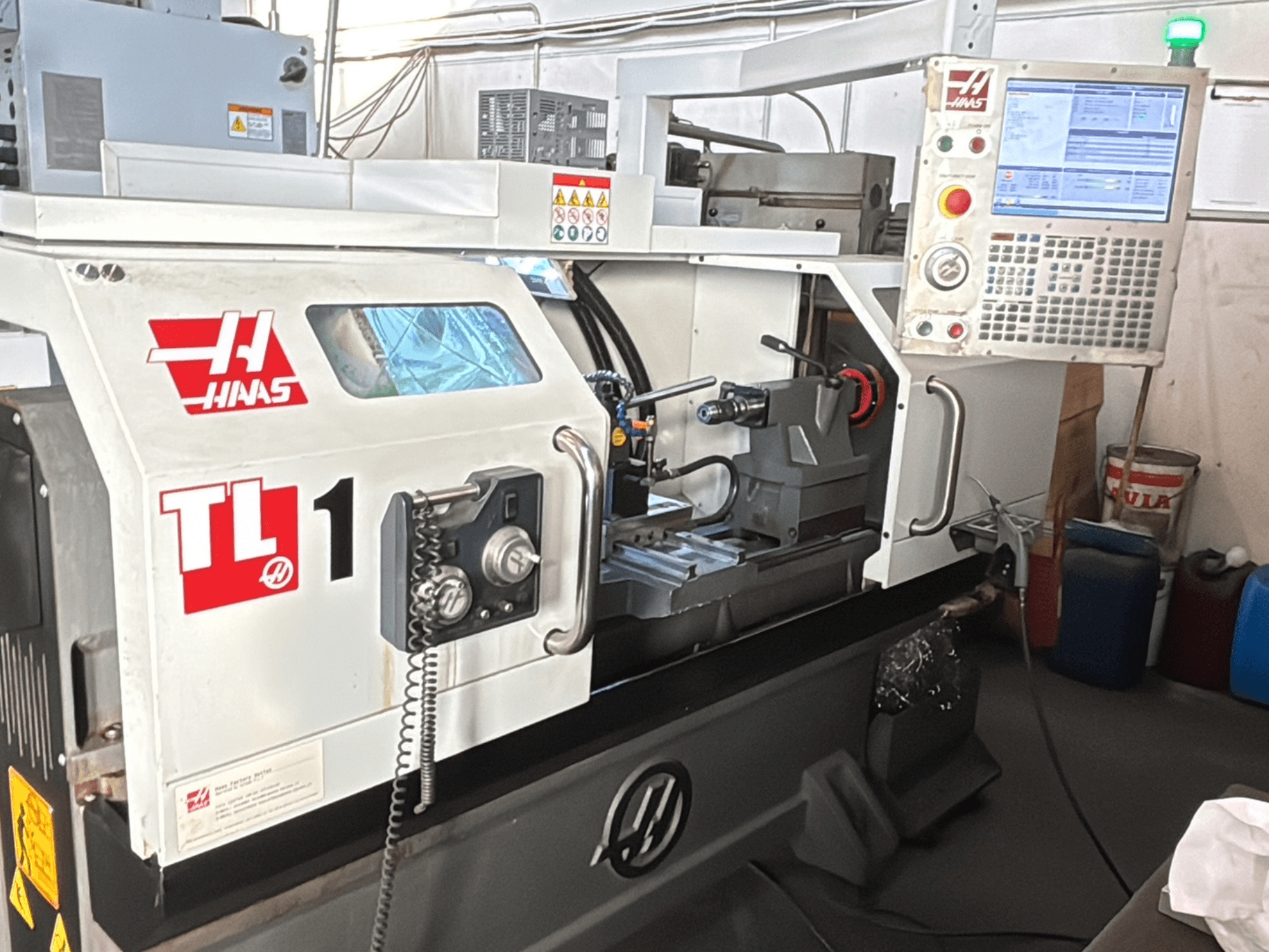 Torno CNC TL-1 de Haas, vista frontal, con panel de control con pantalla, portaherramientas y etiquetas de seguridad.