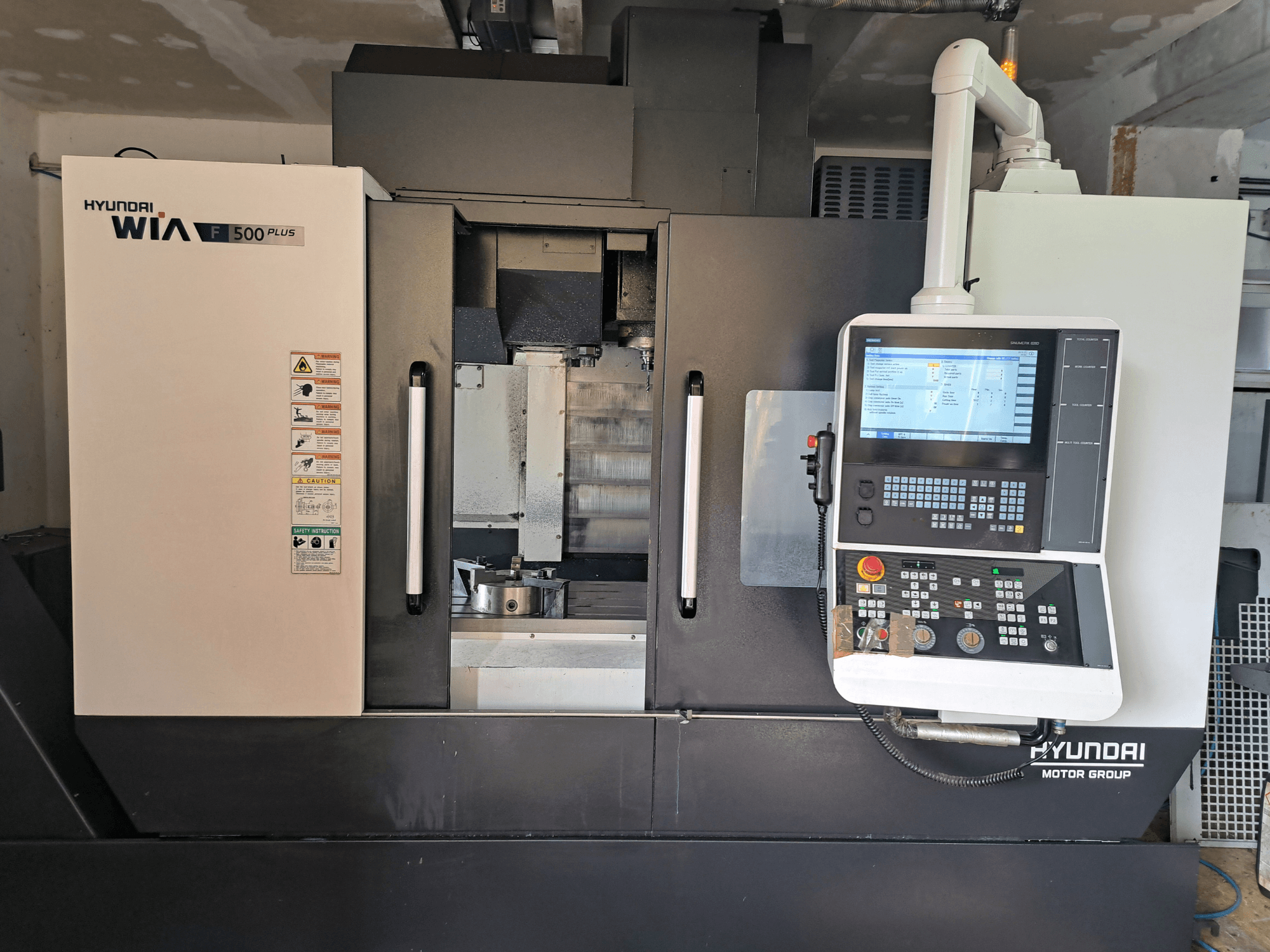 Máquina CNC Hyundai WIA F500 Plus en vista frontal, con panel de control digital y etiquetas de seguridad.