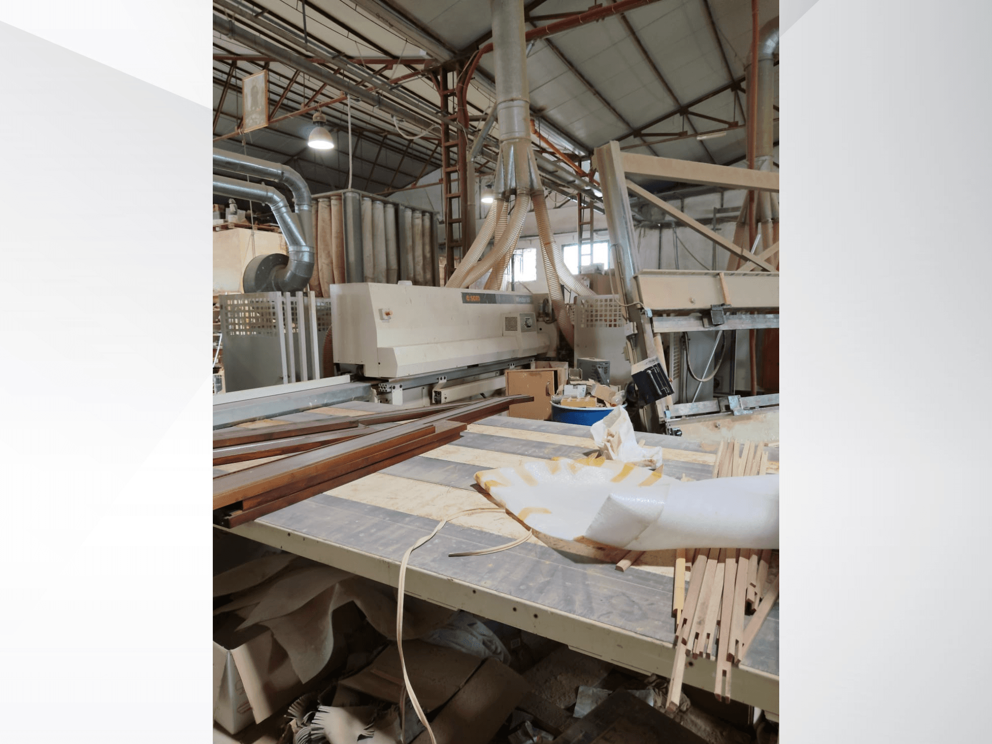 Centro de mecanizado de madera CNC SCM Windor60 en un taller, visto desde el lateral con paneles de madera y equipo de extracción de polvo.