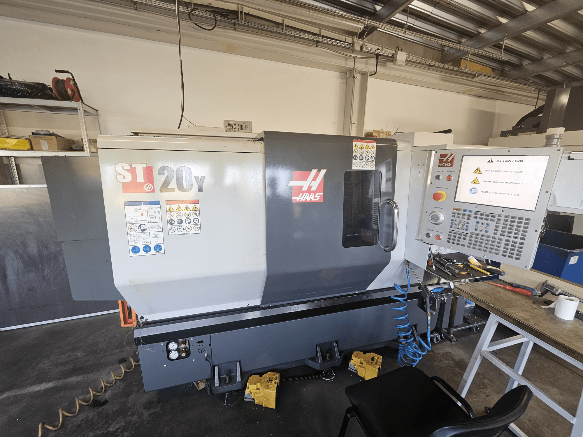 Torno CNC Haas ST-20Y, vista frontal; incluye panel de control, advertencias de seguridad y accesorio para manguera de aire.
