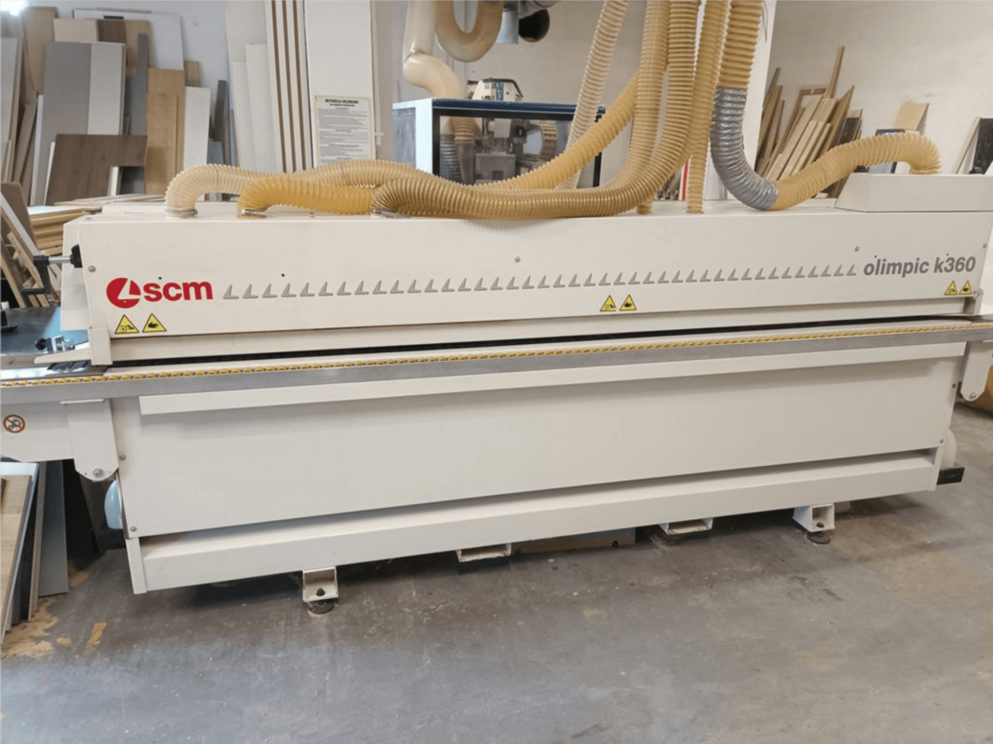 Máquina encintadora SCM Olimpic K360 T-ER1 en un taller; vista frontal en la que se aprecian las mangueras de aspiración de polvo y las etiquetas de advertencia.