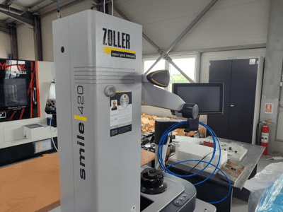 Aparato de medición ZOLLER smile 420 con monitor, vista lateral en un taller, con mangueras azules y maquinaria al fondo.