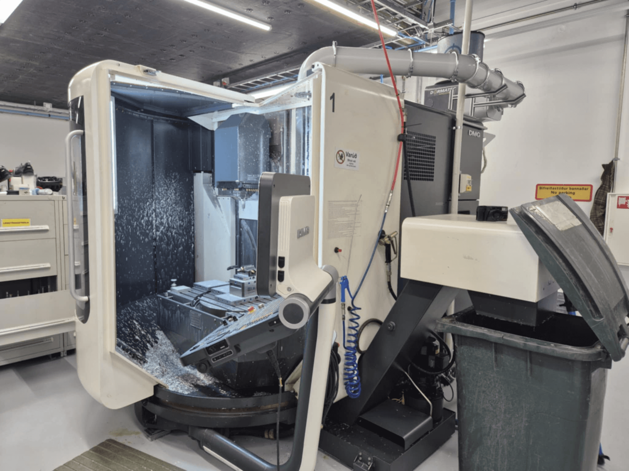 Fresadora DMG abierta con pulverización de refrigerante, mostrando las virutas de metal y los controles de la herramienta, vista de frente.