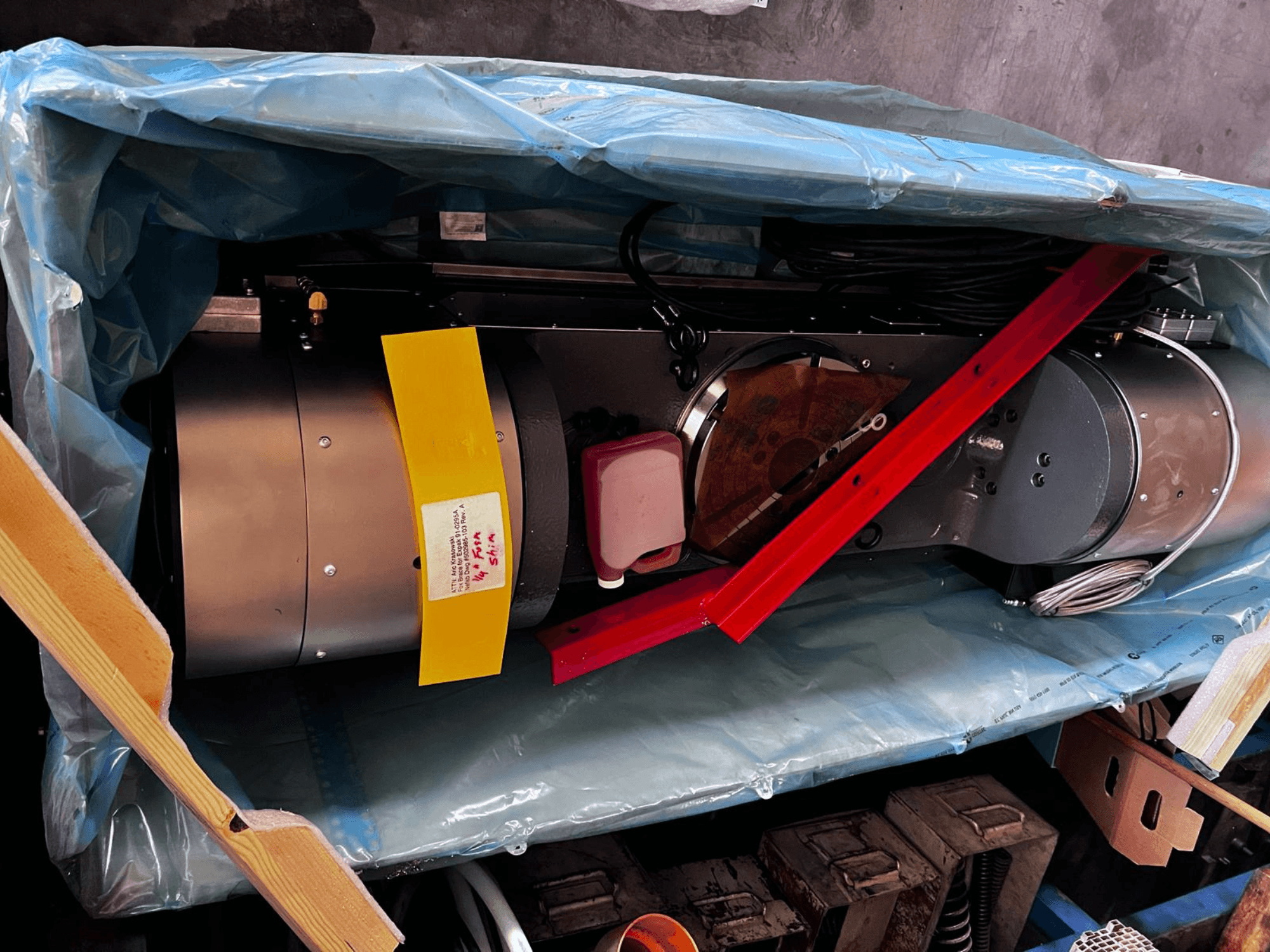 Dispositivo motor parcialmente visible en el embalaje, presenta un exterior plateado, indicadores de colores y una abrazadera de soporte roja.