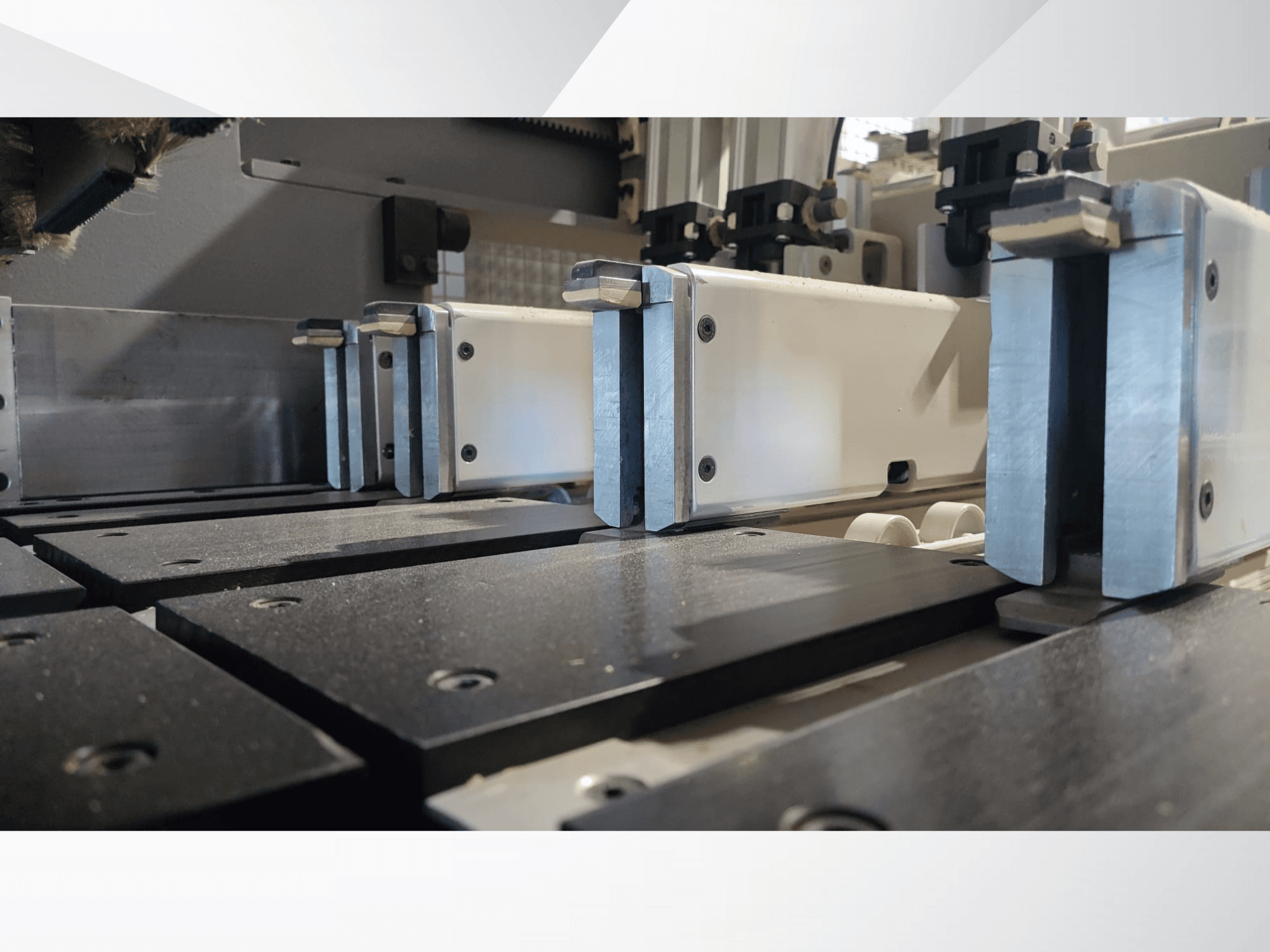 Primer plano del mecanismo de sujeción de una máquina de precisión con mordazas metálicas, con superficies de trabajo negras y carriles guía visibles.