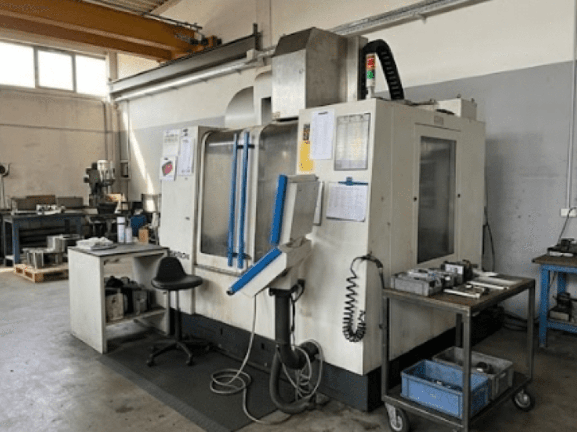 Centro de mecanizado vertical MIKRON VCE 1000 Pro en un taller, vista frontal con detalles en azul y mesa de trabajo adyacente.