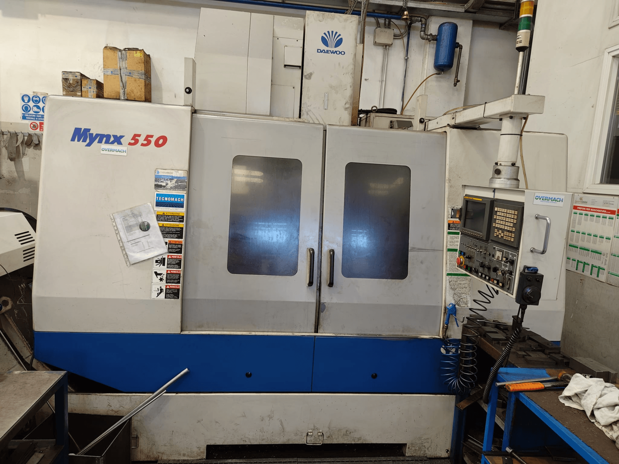 Centro de mecanizado vertical DAEWOO MYNX 550, vista frontal, en la que se aprecian el panel de control, dos puertas grandes y las etiquetas de seguridad.