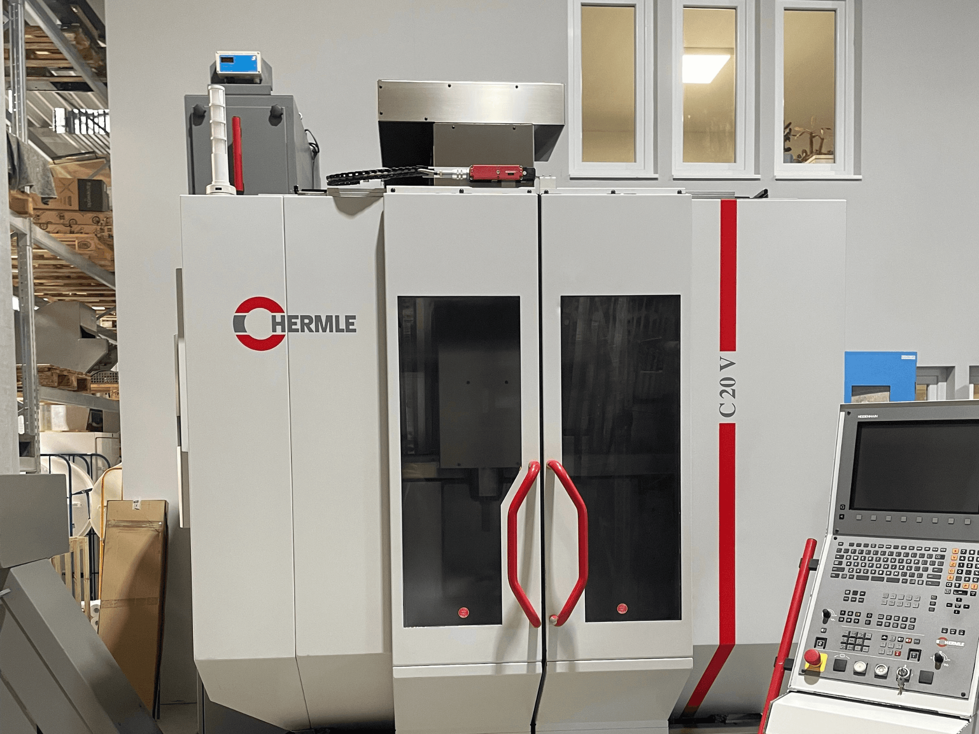 Máquina CNC Chermle C20 V, vista frontal, con panel de control y asas rojas; diseño industrial con grandes puertas de cristal.
